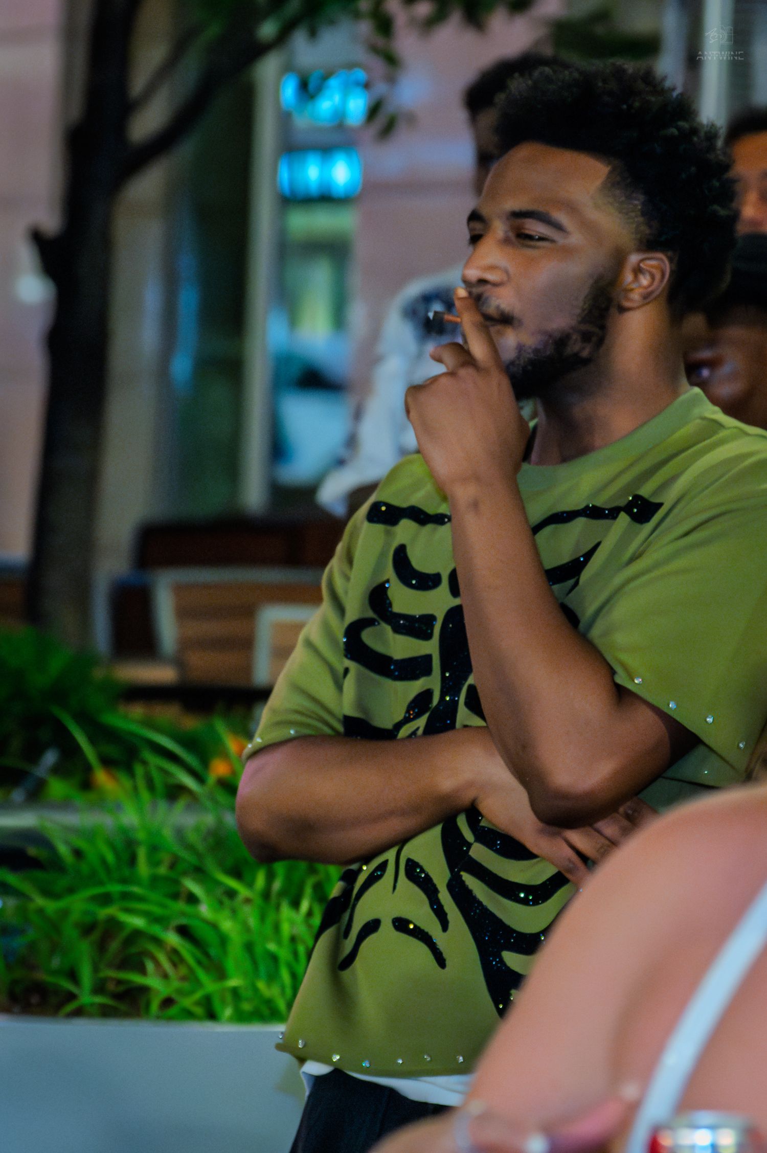 Man in olive green zebra print shirt smoking at outdoor evening gathering.