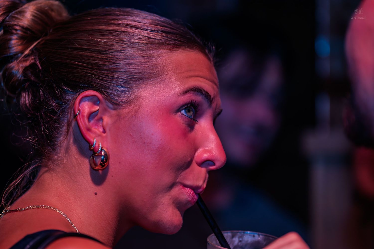 Close-up profile of a woman drinking through a straw at a nightclub event.