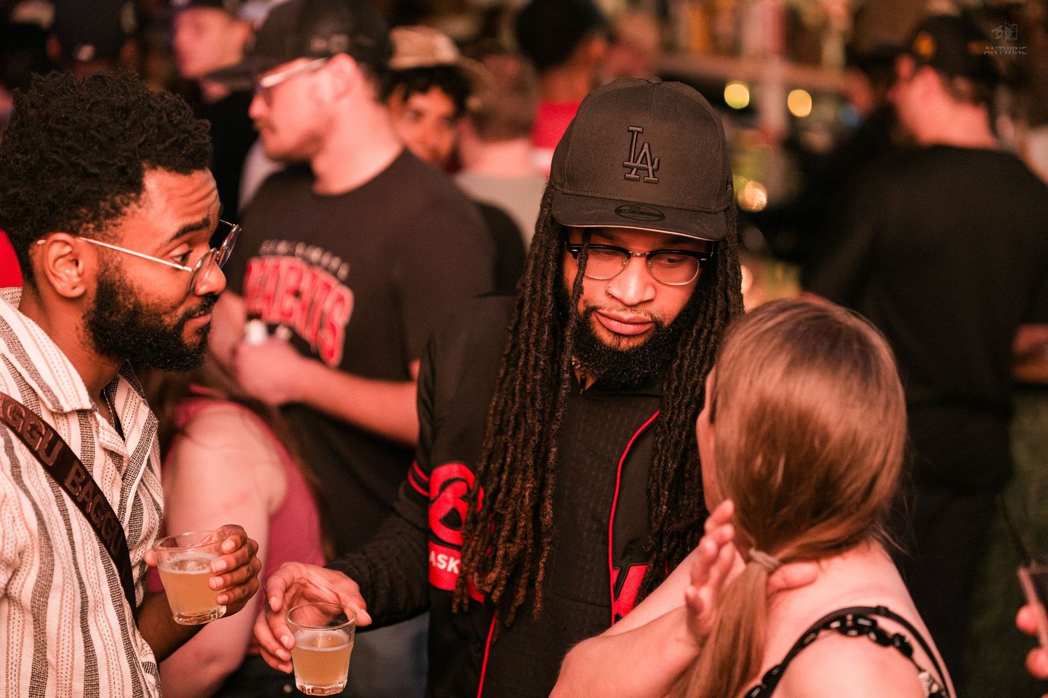 Three people socializing and holding drinks at a busy nightclub event.
