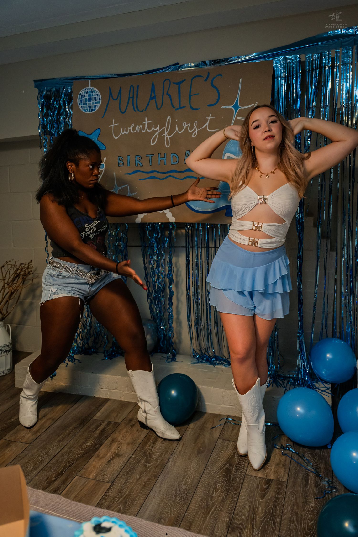 Two women dance together at Malarie's 21st birthday party with blue balloons and tinsel backdrop.