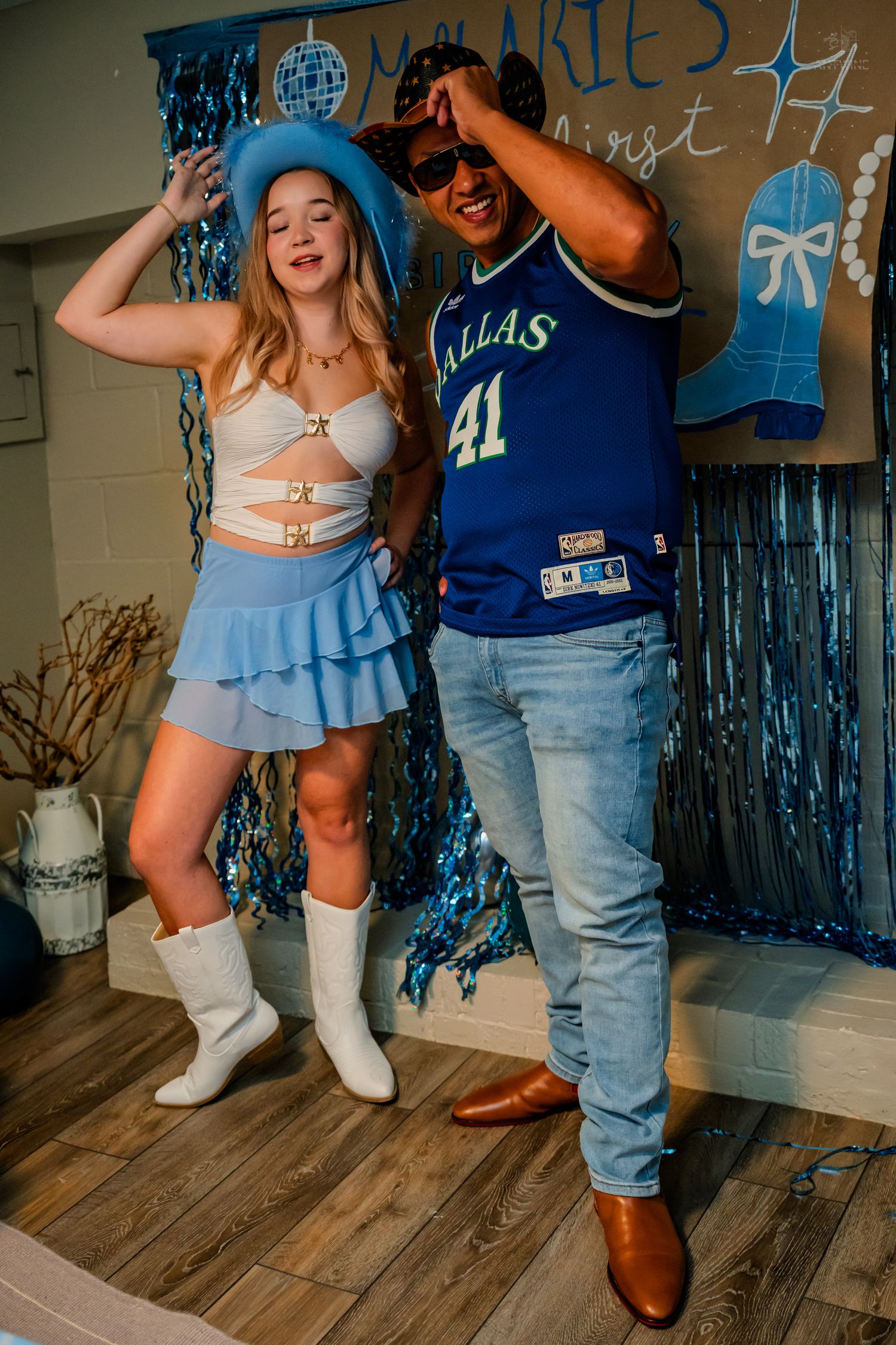 Woman in blue cowboy hat dances with man in Dallas 41 jersey at blue-themed birthday party.