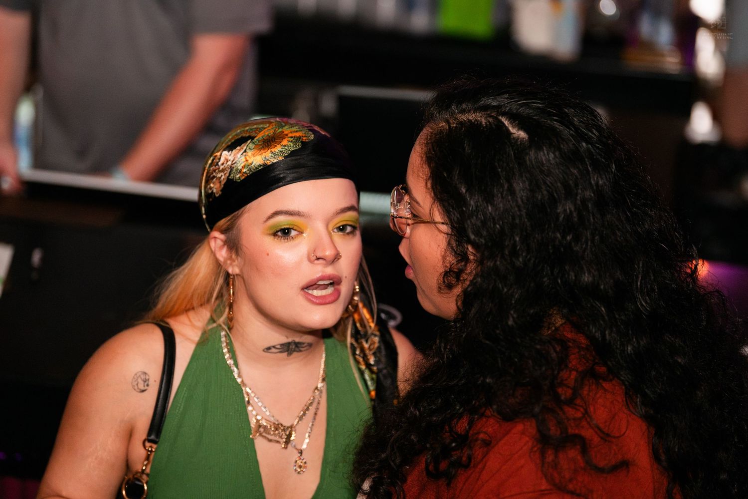 Two women having an intimate conversation at a bar or nightclub event.
