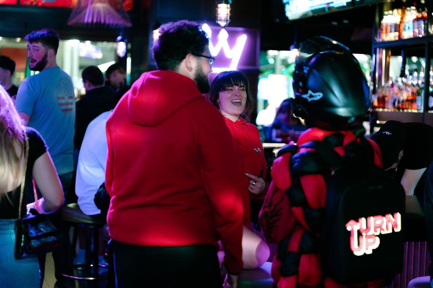 Group of people socializing inside colorful nightclub with neon lighting and bar seating.