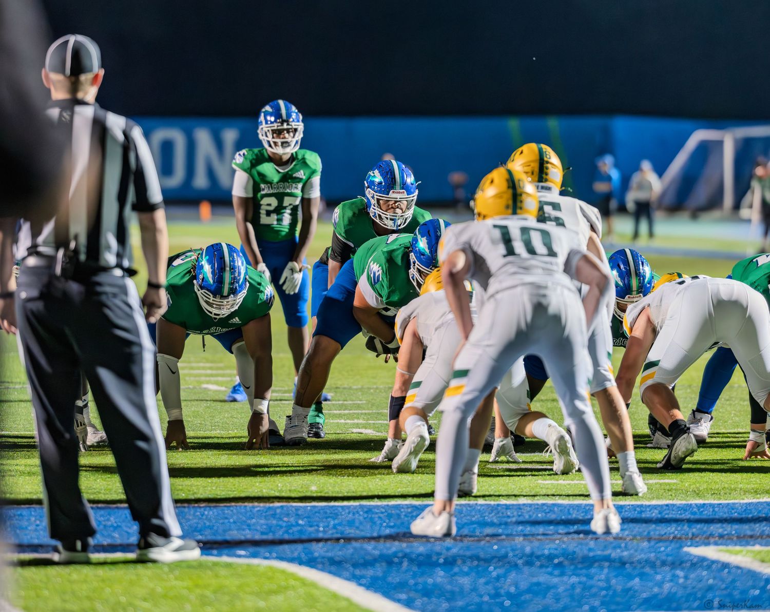High school football teams line up at goal line during close nighttime game situation.