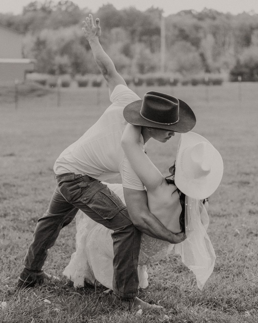 Black and white photo of groom dipping bride dramatically in a field during their outdoor wedding celebration.