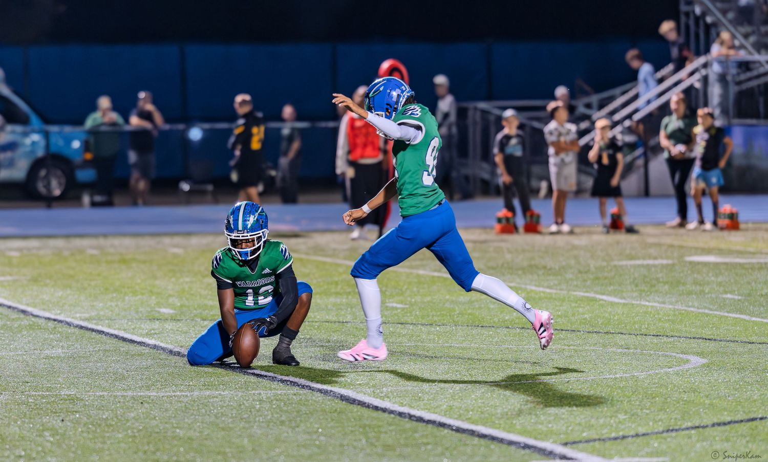 Warriors football player attempts a field goal kick during a night high school football game.