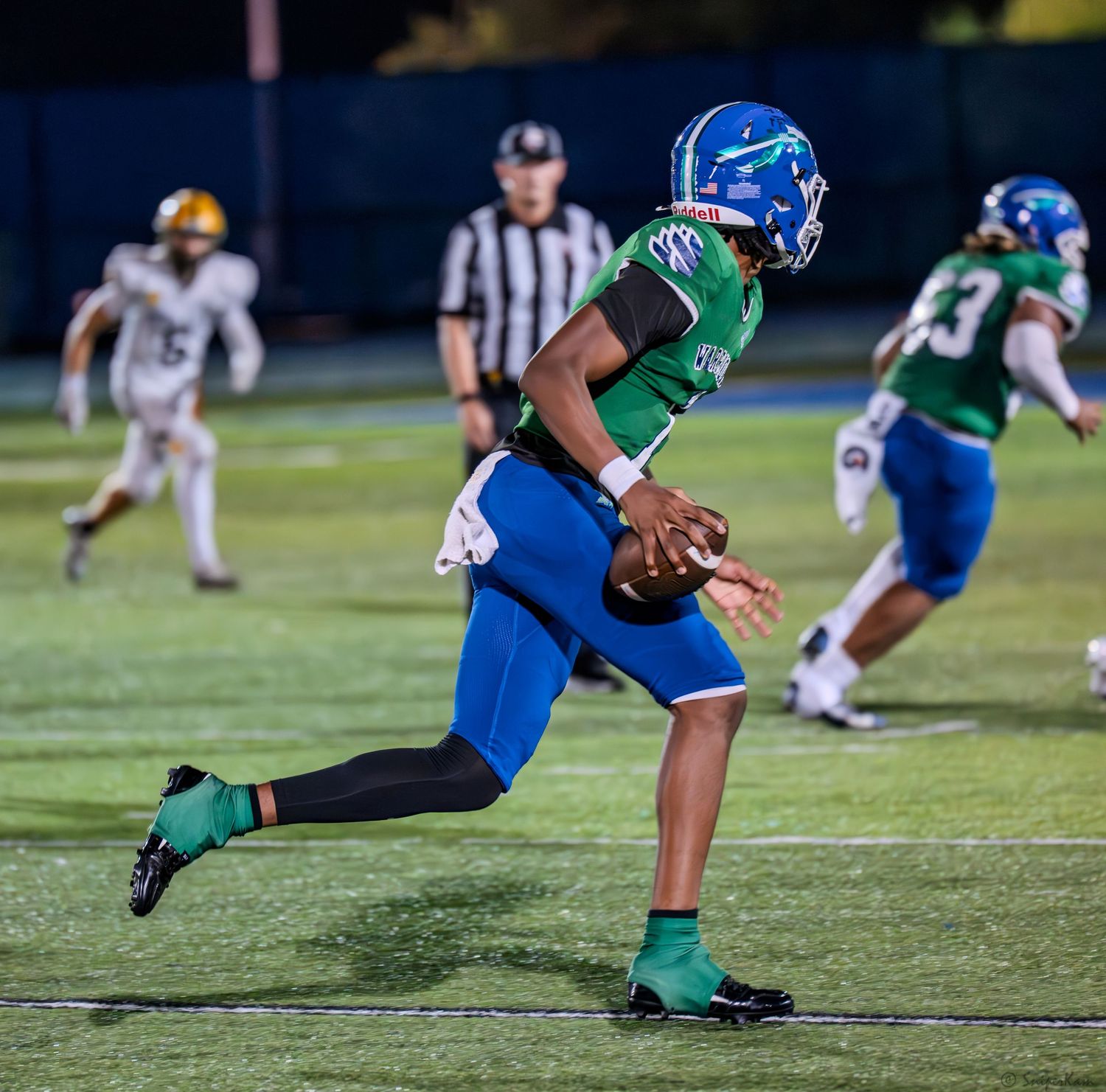 A football player in green uniform carries the ball during a high school night game.