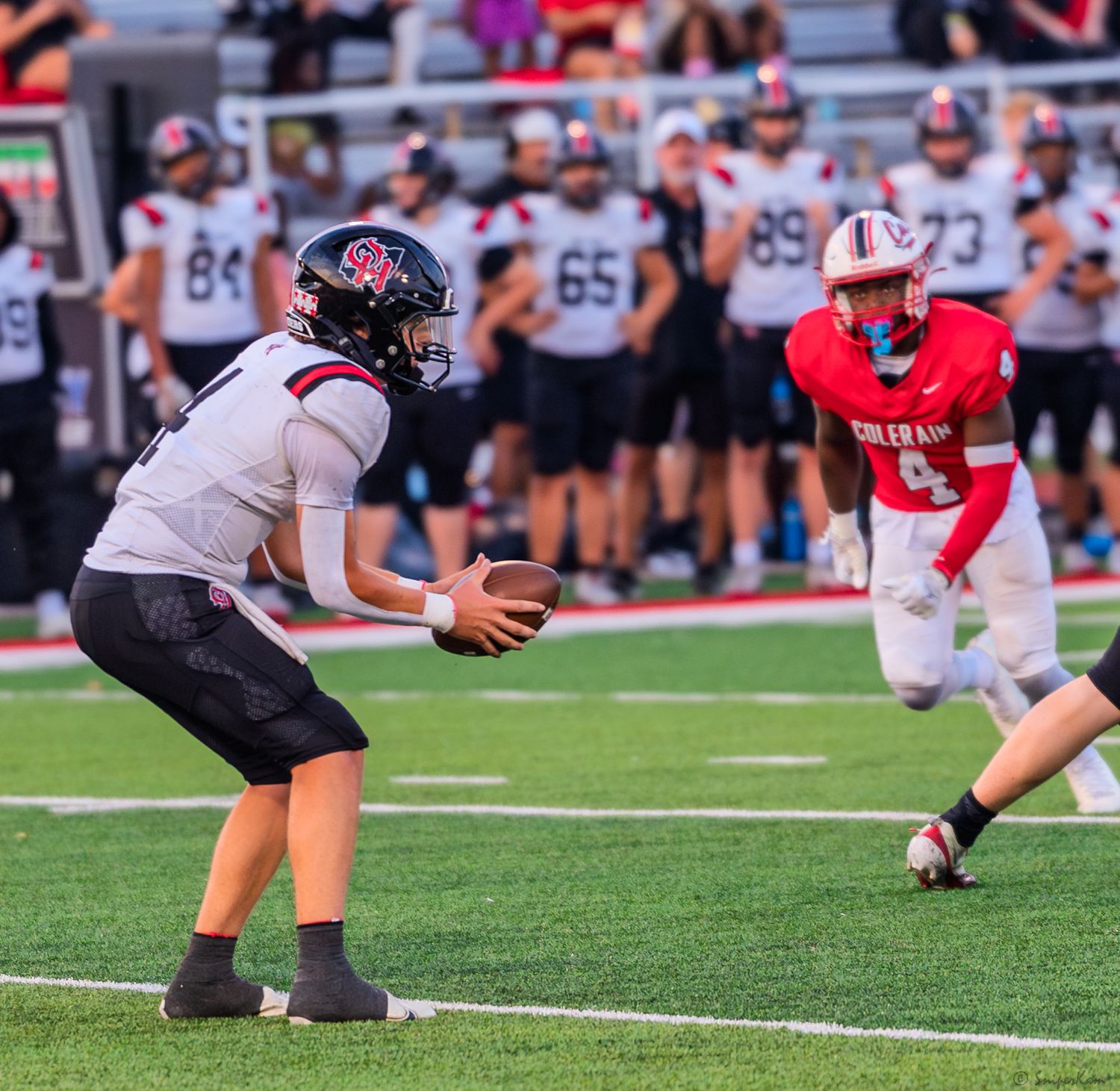 Football player in white uniform catches a snap during a high school game with defender in red pursuing.