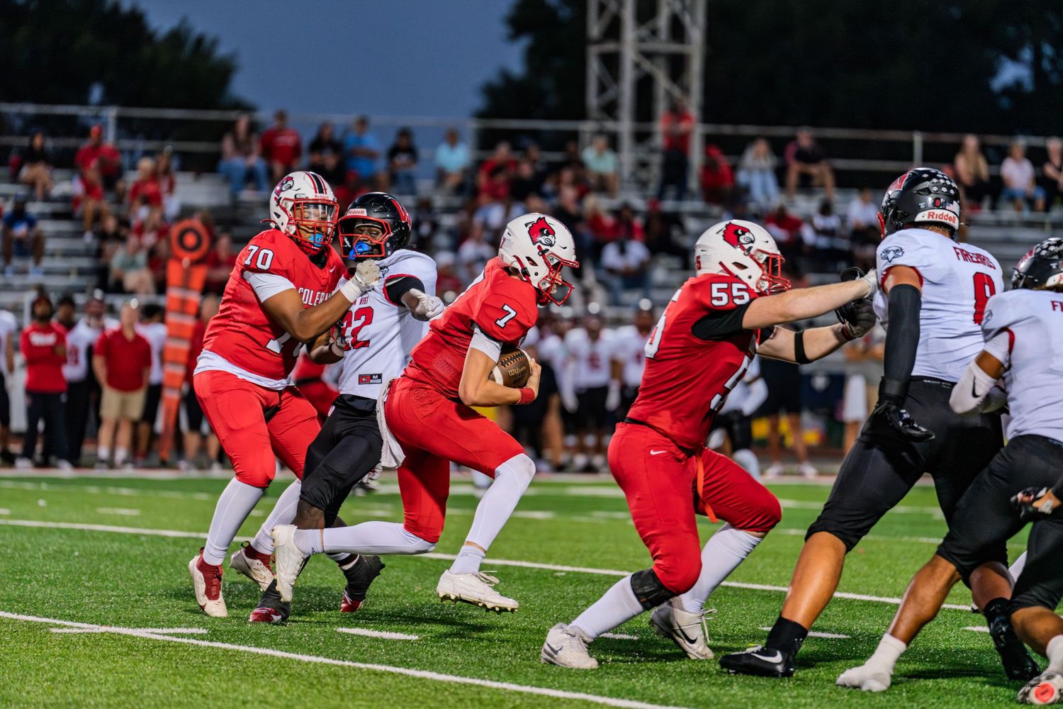 Red team quarterback #7 hands off ball to running back during a high school football game.