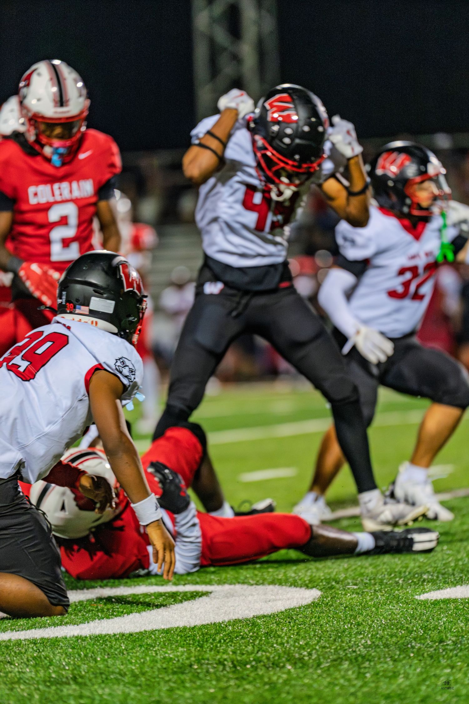 White-uniformed football players celebrate a tackle on a red-uniformed ball carrier during a night game.