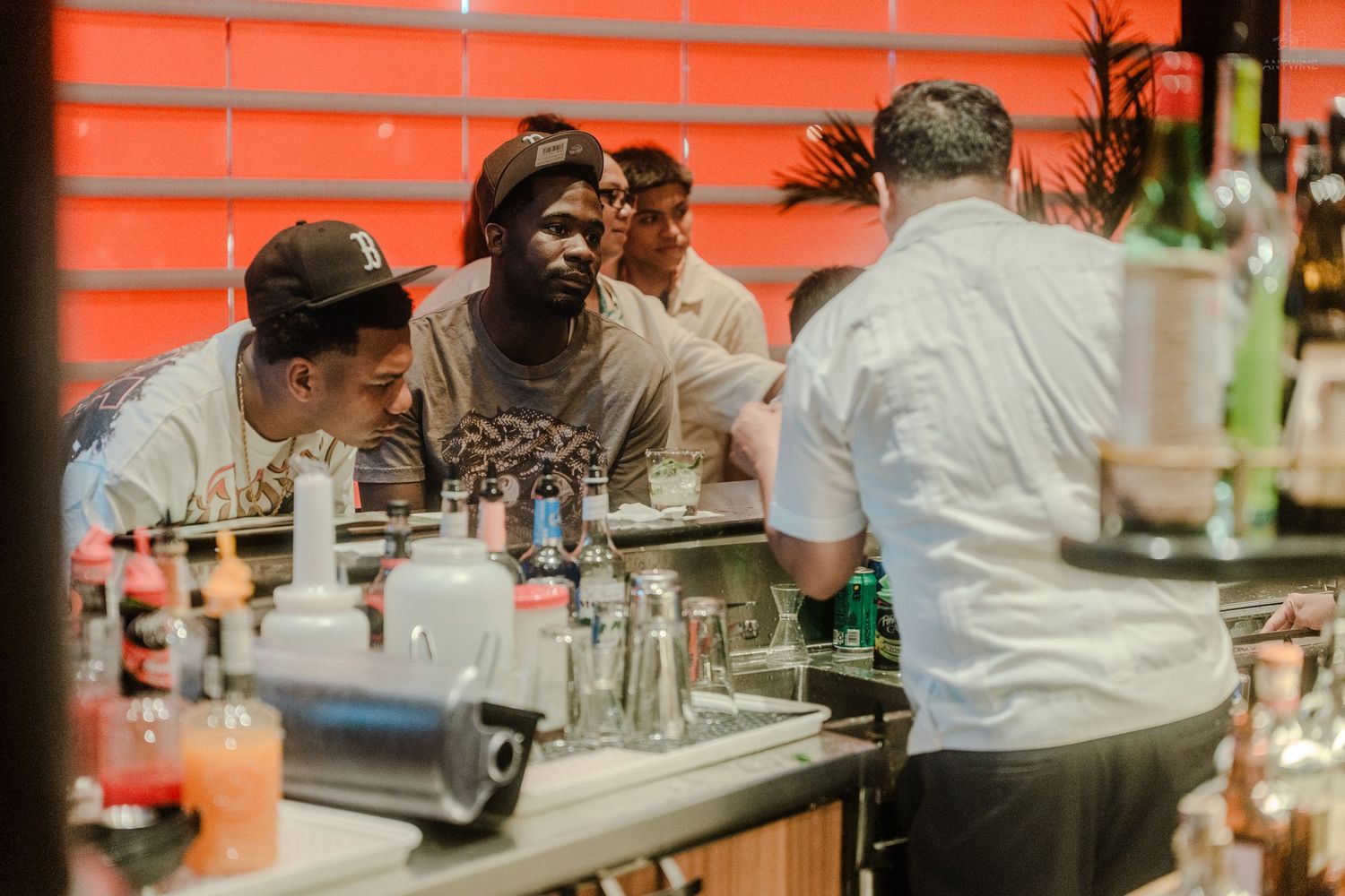 Two guests chat with a bartender at a vibrant red-lit bar on a cruise ship.