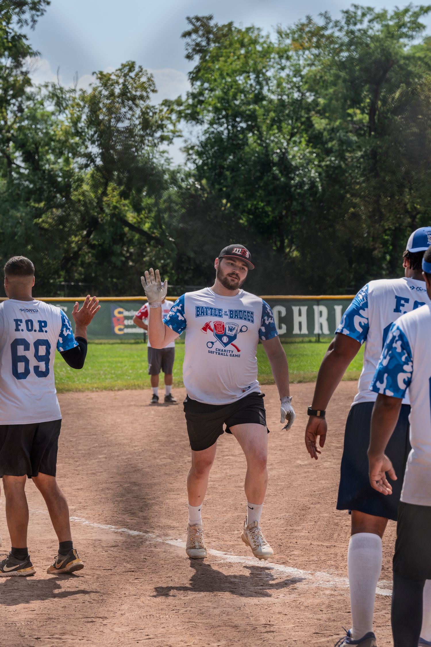 Player in Battle of the Badges softball jersey high-fives teammates after scoring a run on a sunny day.