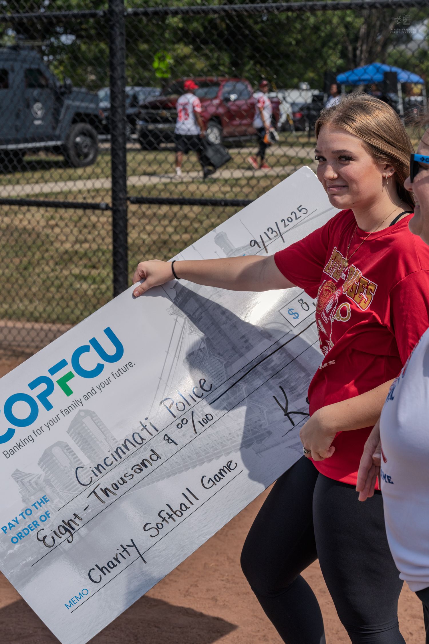 Young woman holds large COPFCU check for eight thousand dollars donated to Cincinnati Police charity softball game.