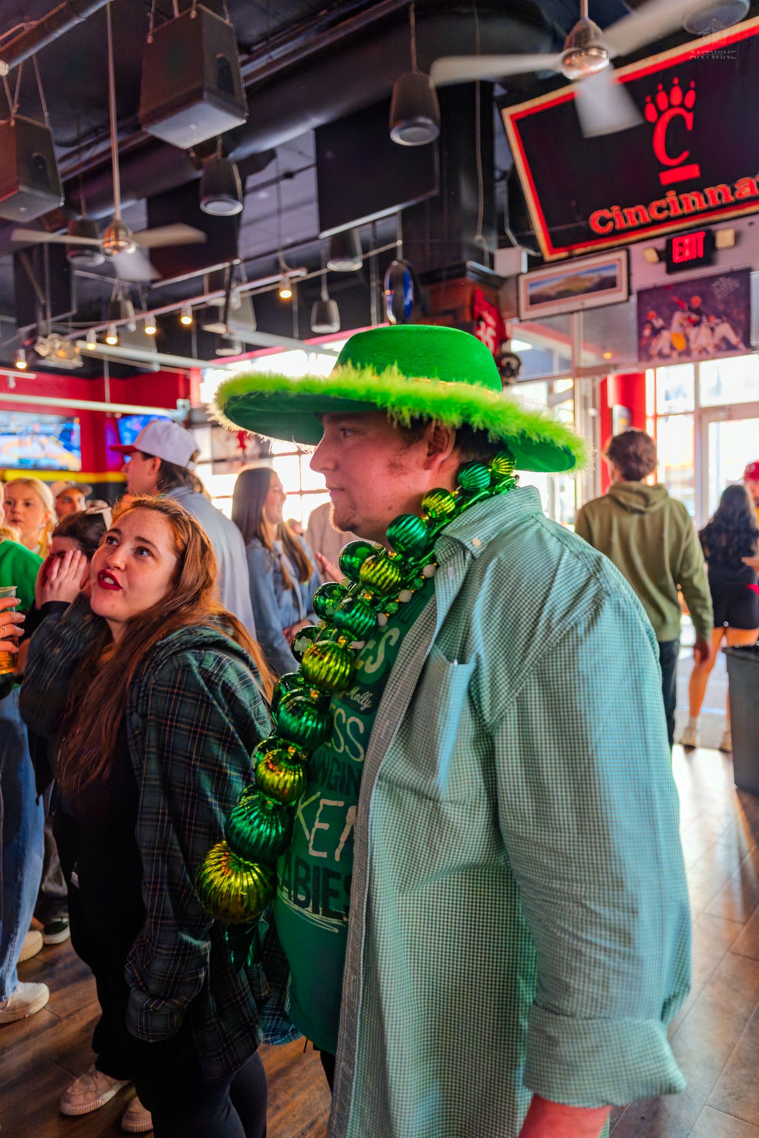 Man in green St. Patrick's Day hat and bead necklace at a Cincinnati bar celebration.