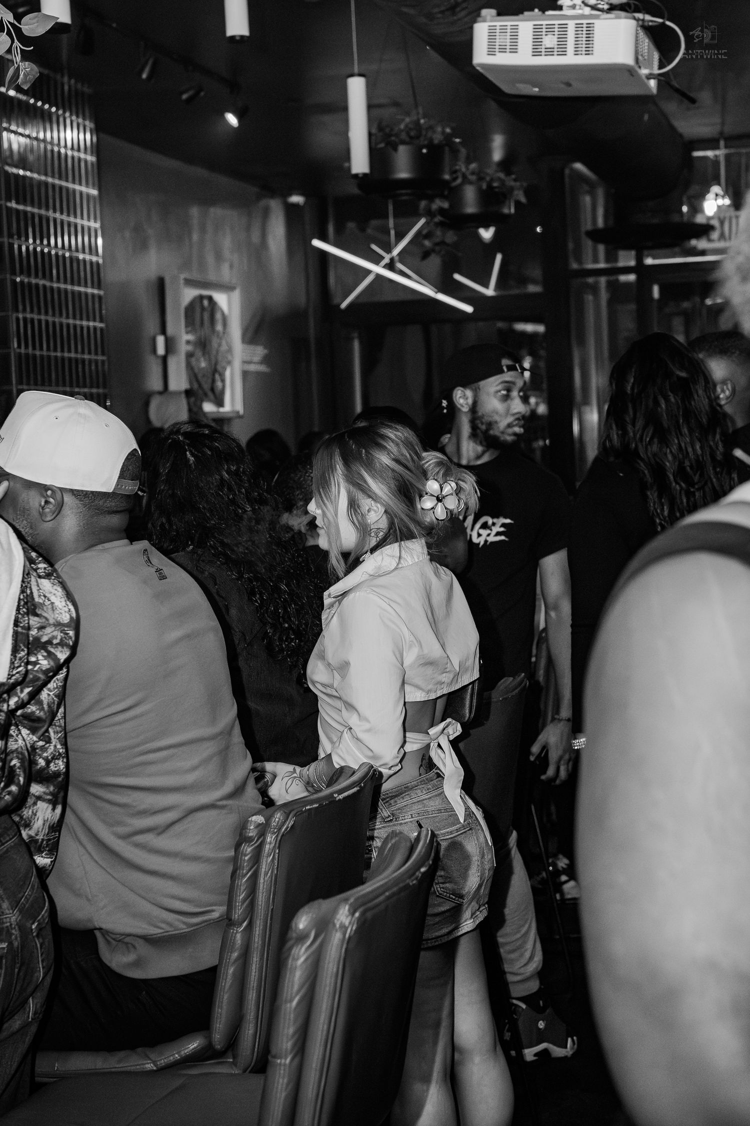 Black and white photo of a crowded bar or nightclub with people socializing in a dimly lit interior.