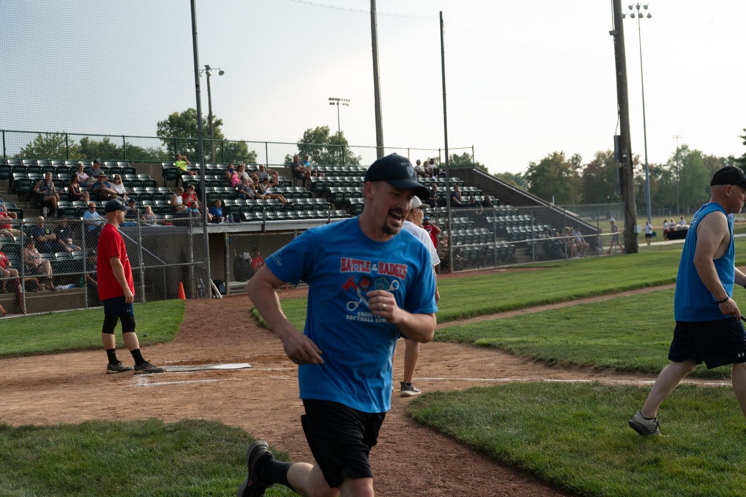 A man in a blue shirt runs the bases at an outdoor baseball field during a recreational game.
