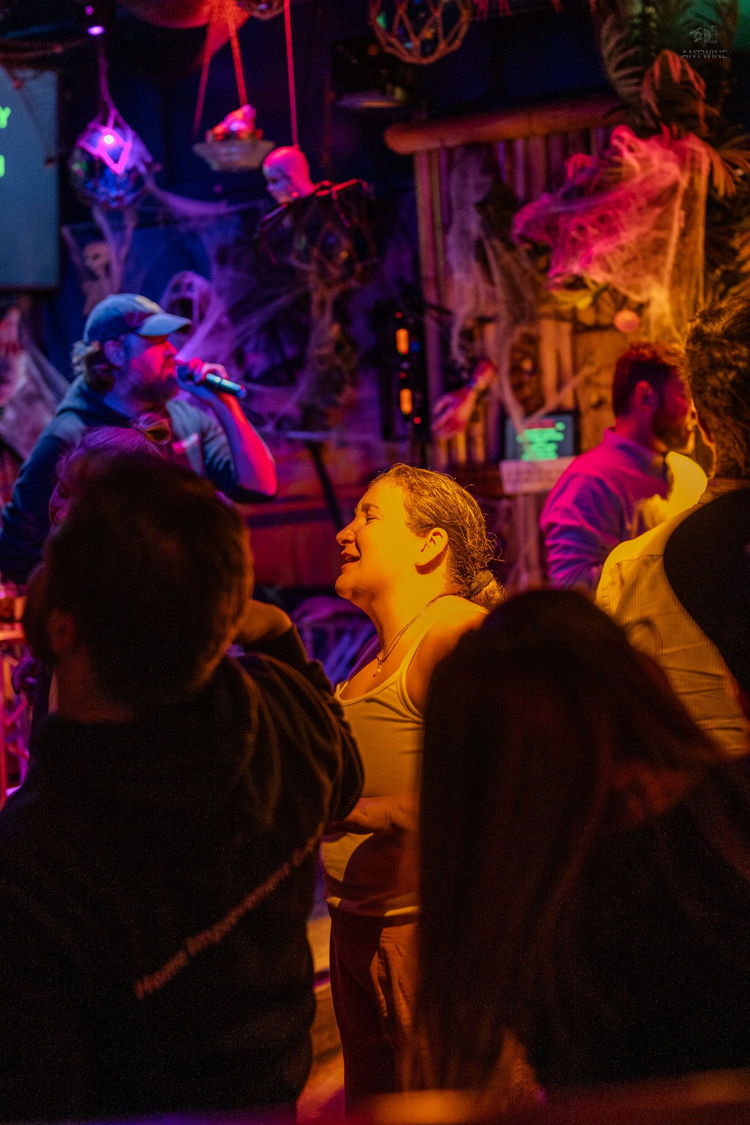 Crowd enjoying live music at a Halloween-themed bar with colorful purple and orange lighting.