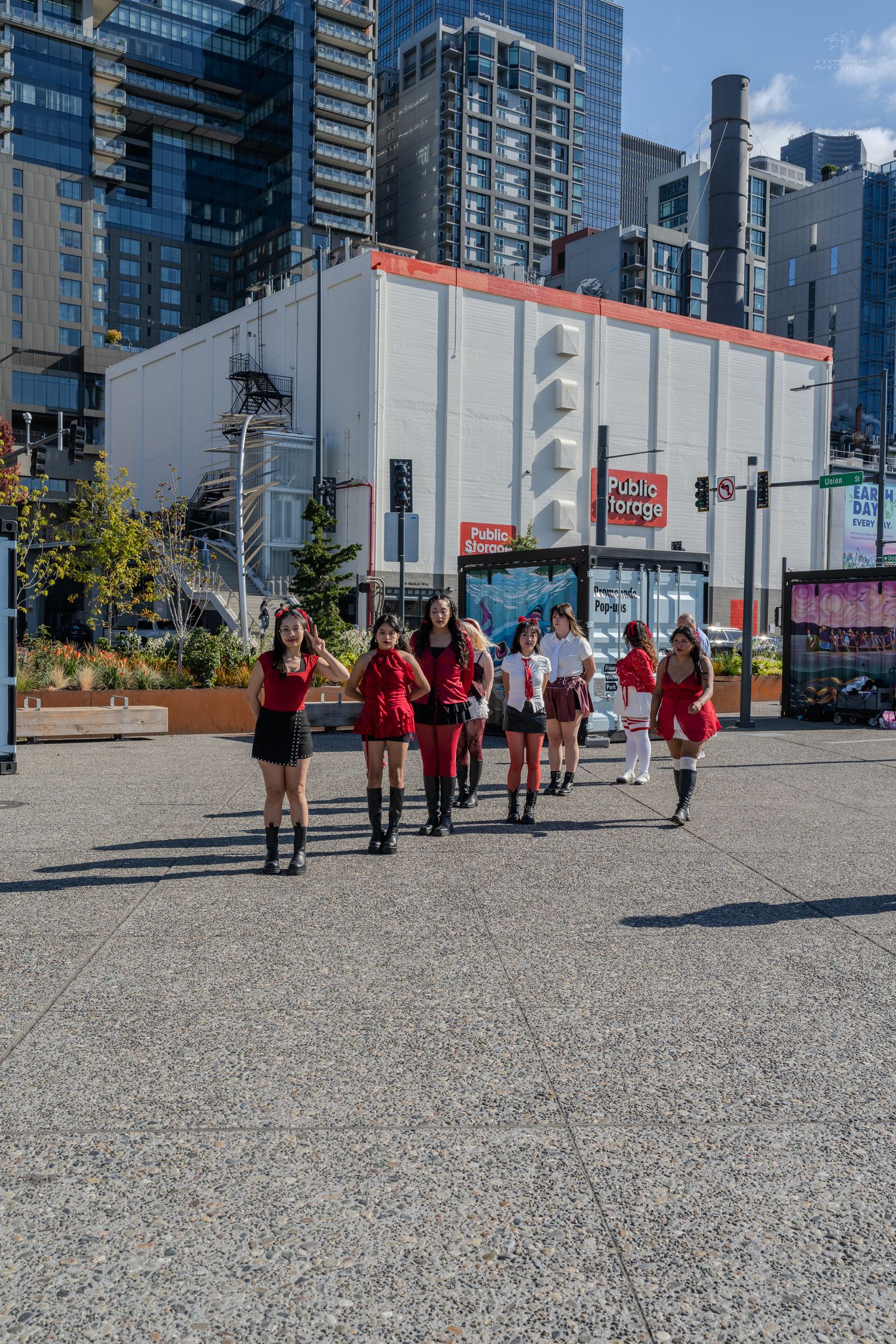 Group of young women in red outfits walking in an urban plaza with city skyscrapers in the background.