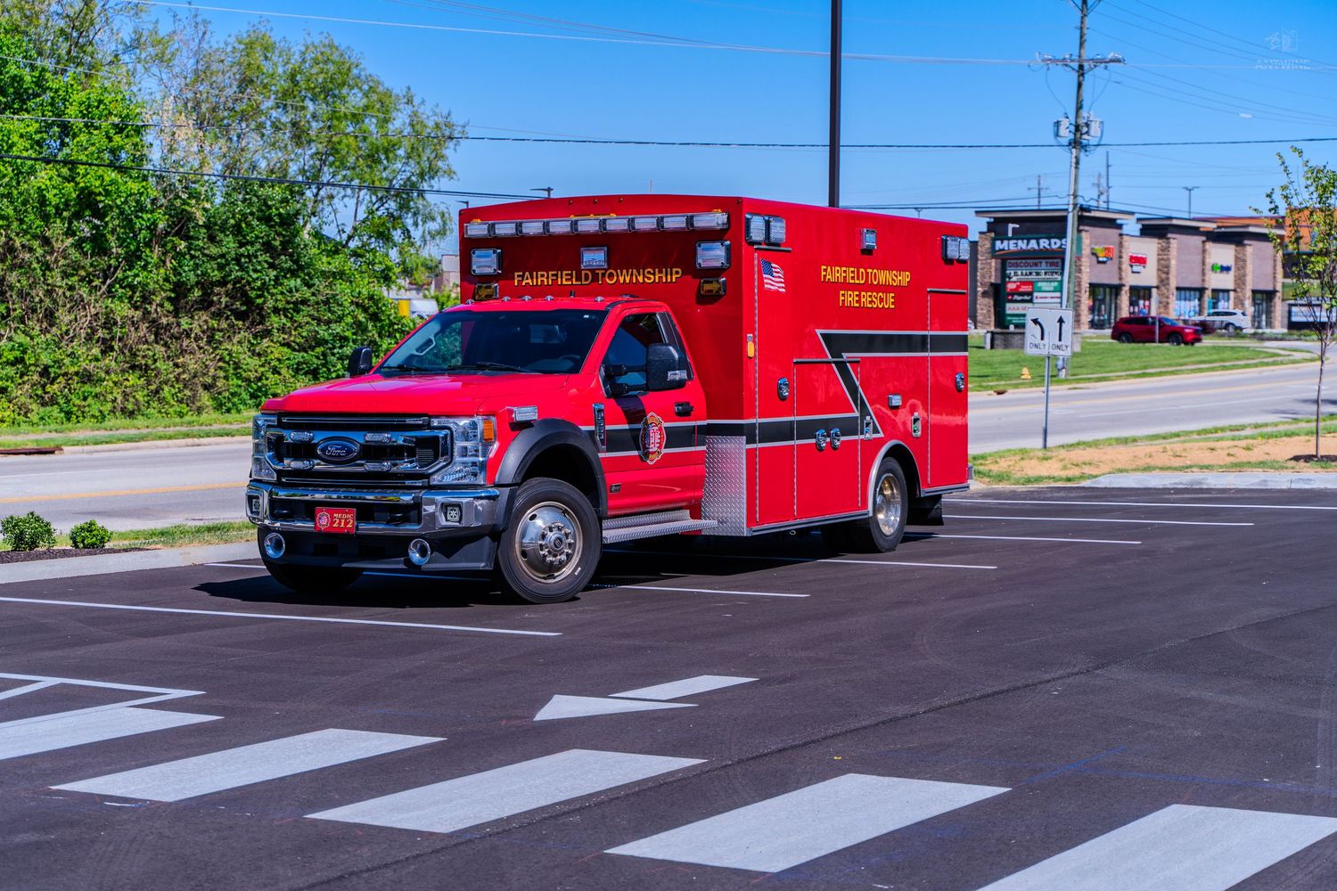 Red ambulance emergency vehicle driving through intersection on sunny day with clear blue sky.