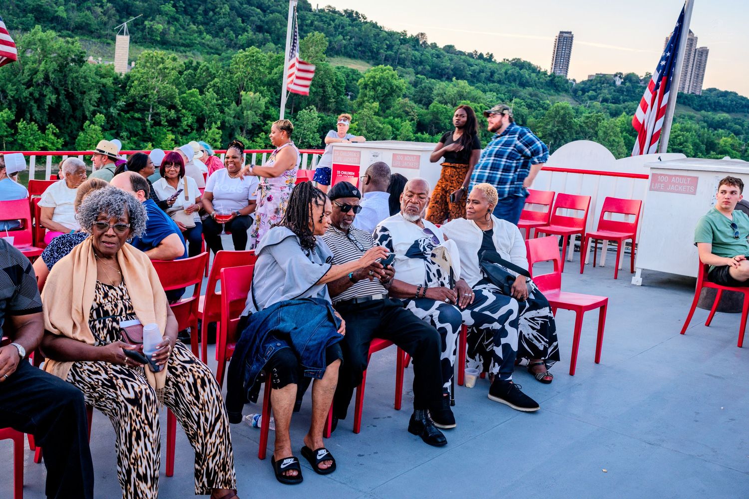 Group of guests seated in red chairs on a boat deck enjoying an outdoor evening river cruise event.