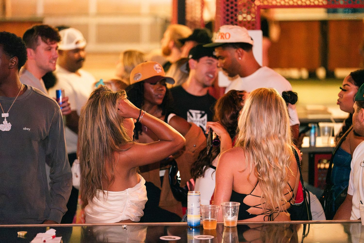 Group of friends socializing and drinking at a busy outdoor bar or nightclub.