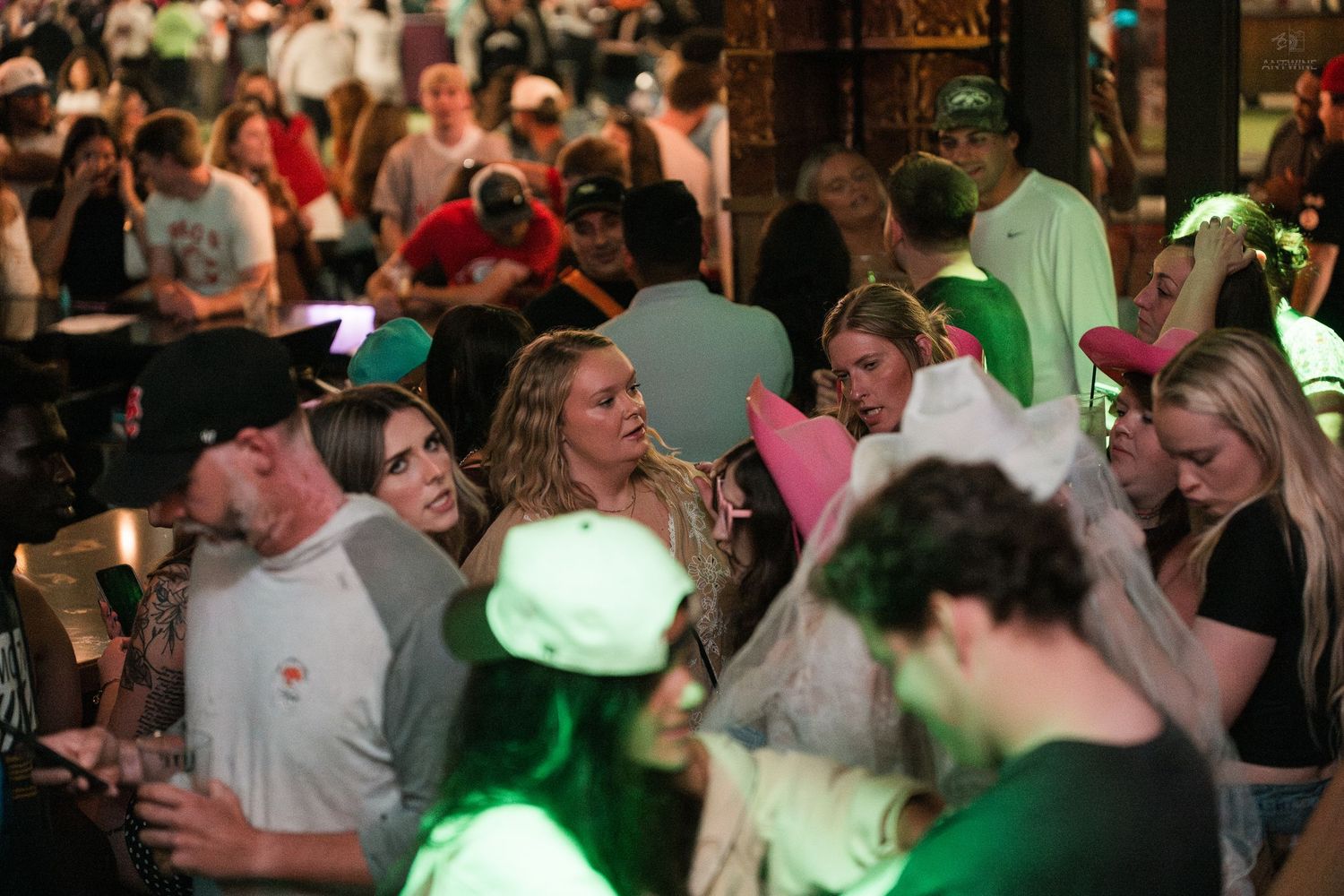 Large crowd of young people socializing under green lighting at a lively outdoor bar event.