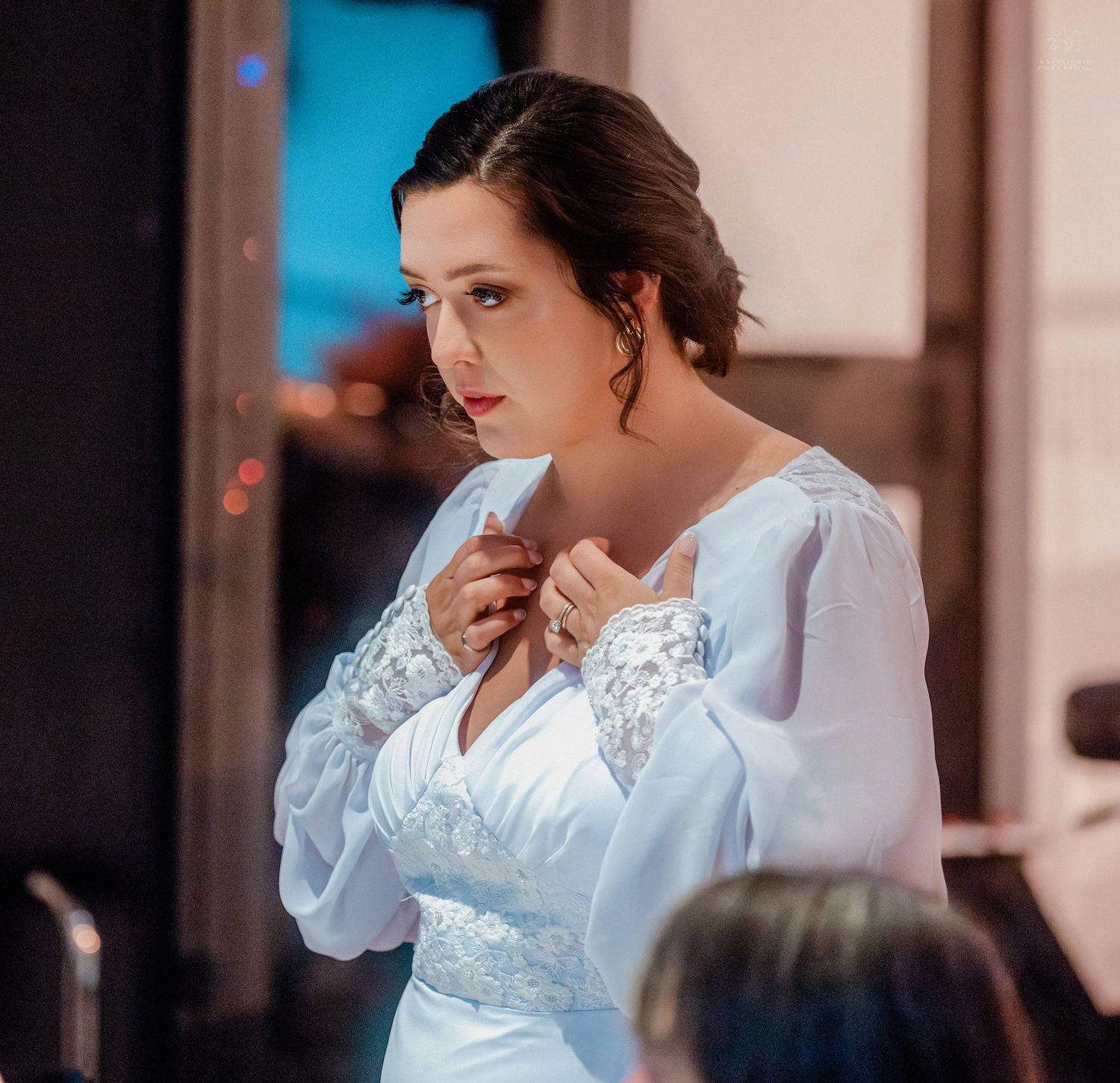 Elegant bride in white lace long-sleeve wedding gown adjusts dress in candid portrait shot.