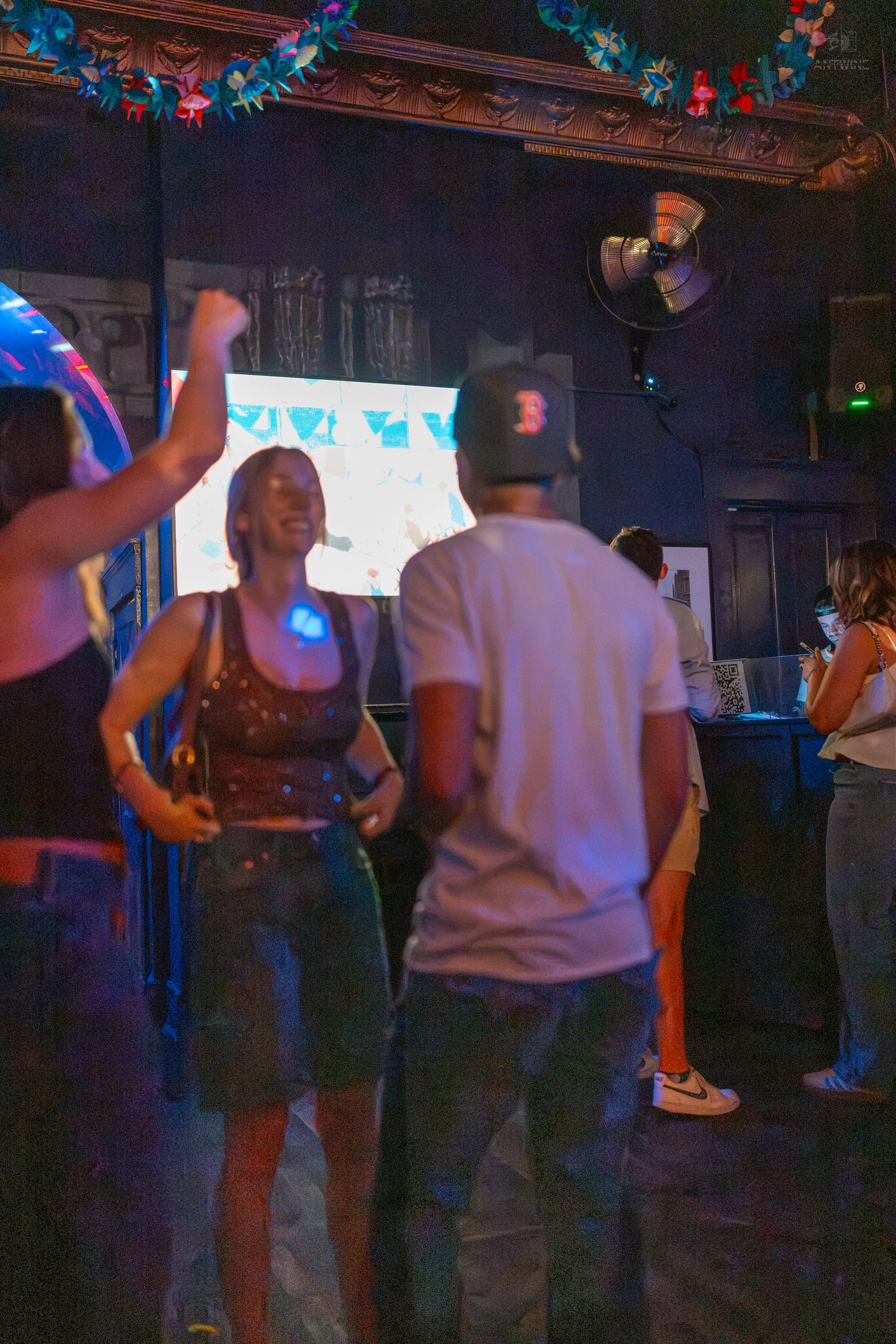 People dancing at a vibrant nightclub party with colorful lights, a projector screen, and festive decorations.