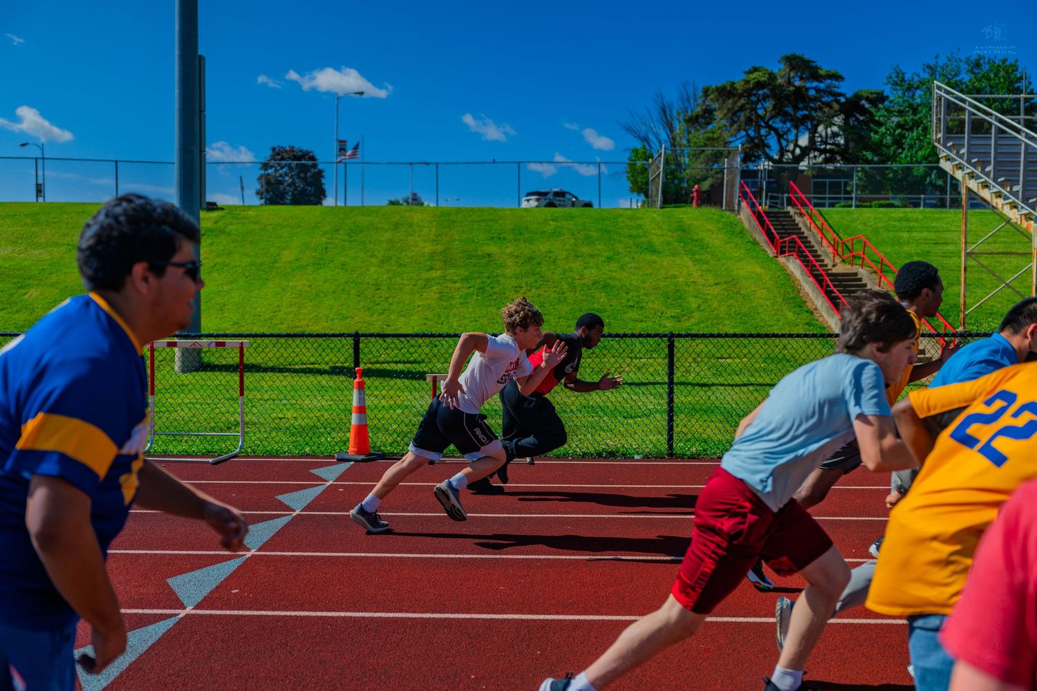 Students racing on a red outdoor track during a school field day event under a bright blue sky.