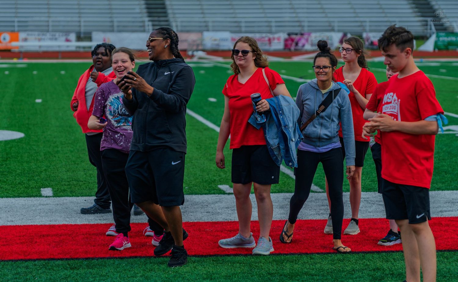 Group of people in red shirts walking on a football field track during an outdoor team event.