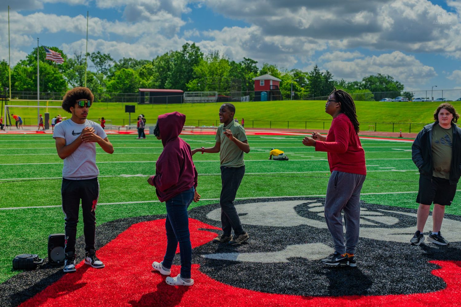 Students gather on a red and black school logo on a football field turf during an outdoor activity.