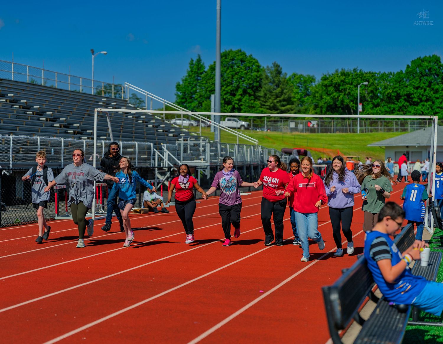 Students walking on a red track at an outdoor stadium on a sunny day during a school event.