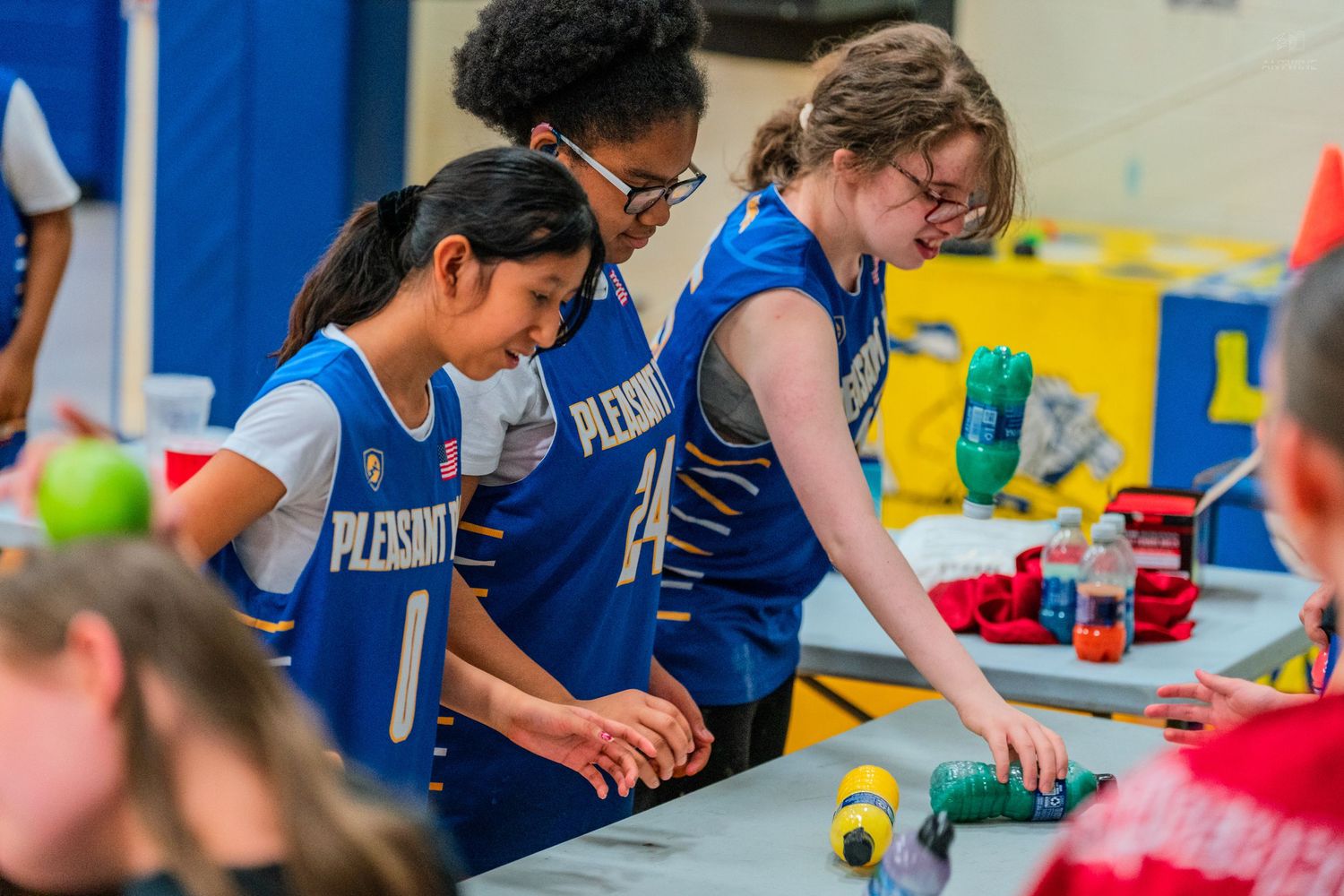 Students in blue Pleasants jerseys collaborate on a hands-on STEM activity at a school science fair event.