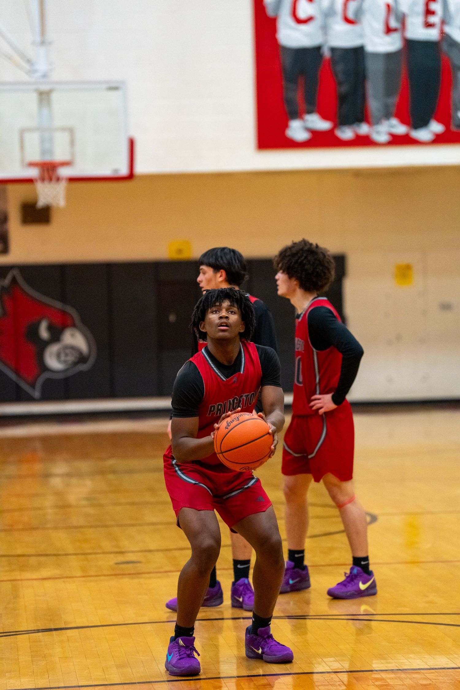 Princeton basketball player prepares for free throw shot while teammates watch in red uniforms on court.