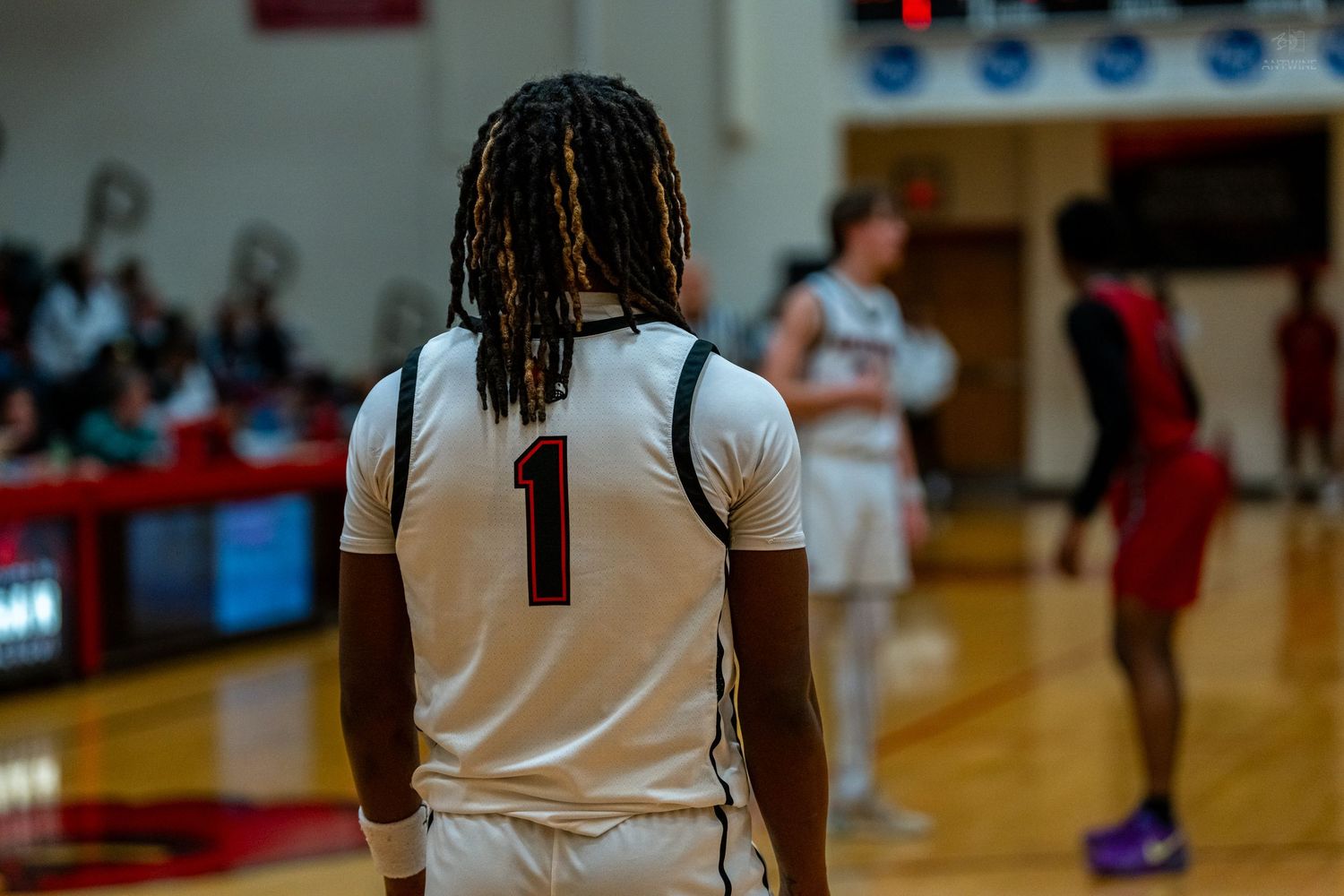 Player wearing jersey number 1 stands on a high school basketball court during a competitive game.