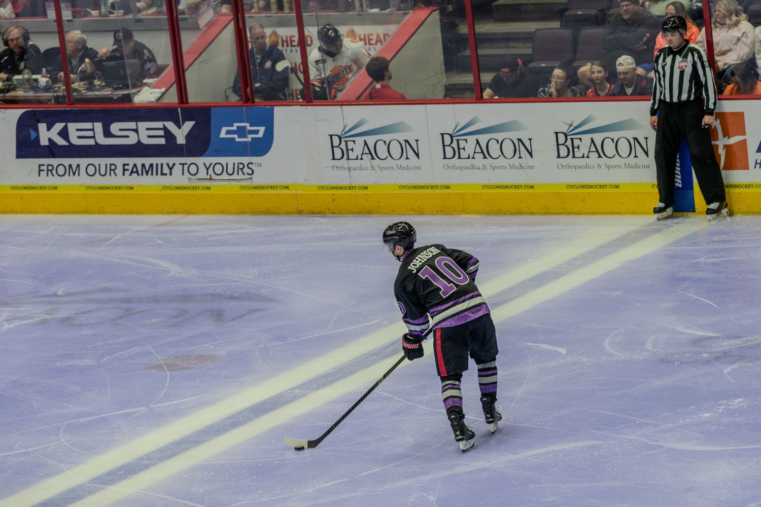 Hockey player wearing number 10 skates with the puck along the boards during a game.