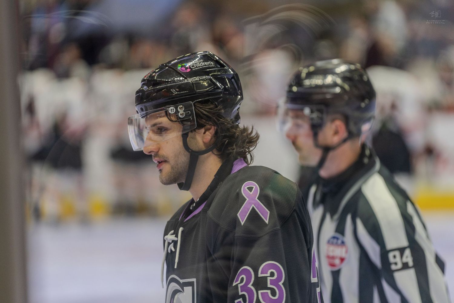 Hockey player wearing number 33 with pink cancer awareness ribbon stands near a referee.