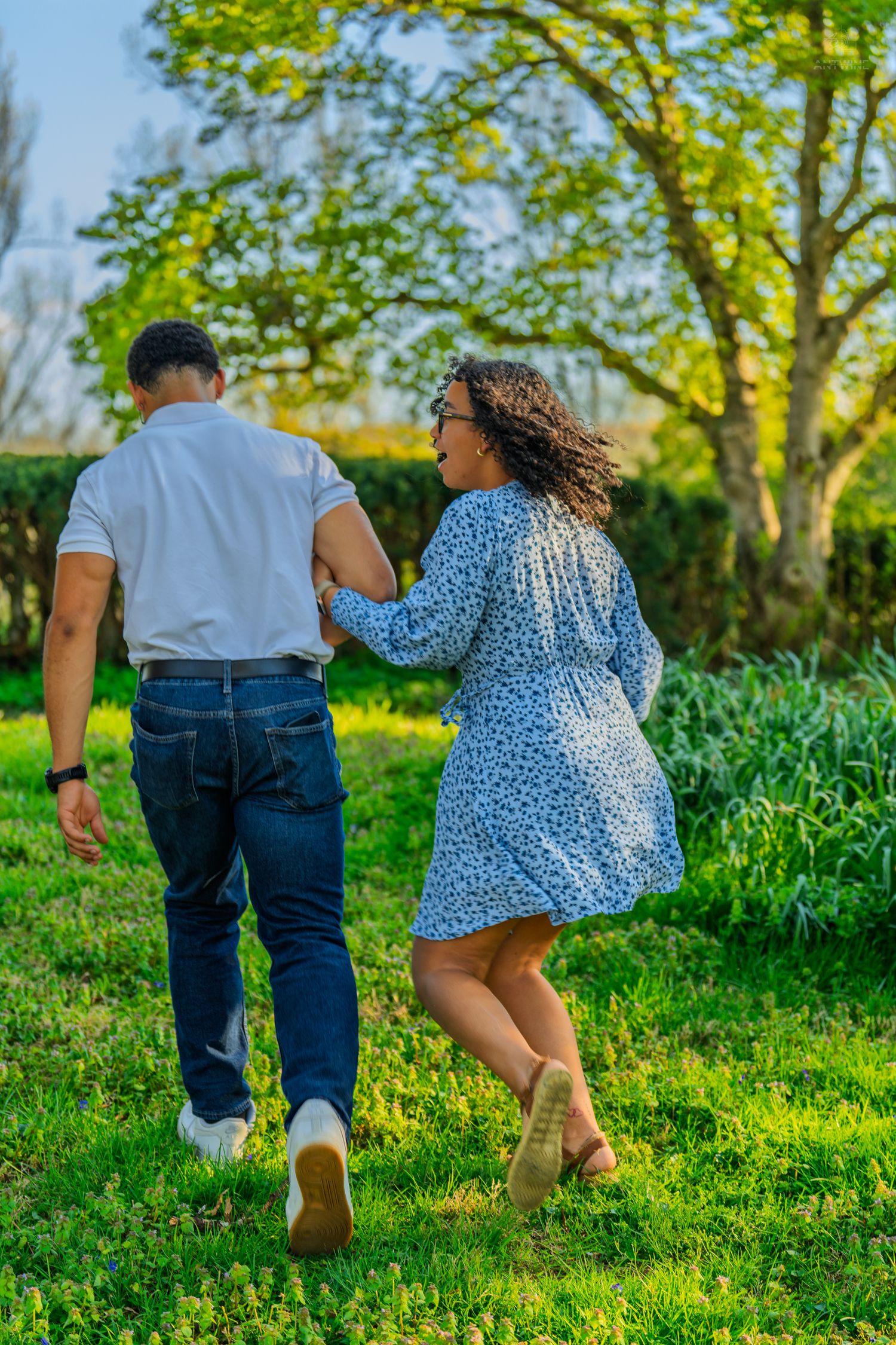 Couple walking arm in arm through a sunny green park, woman smiling joyfully.
