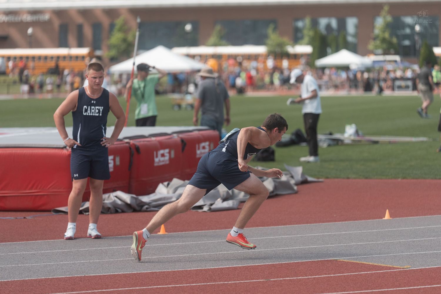 Male track athlete in Casey uniform sprints on red track during outdoor competition.
