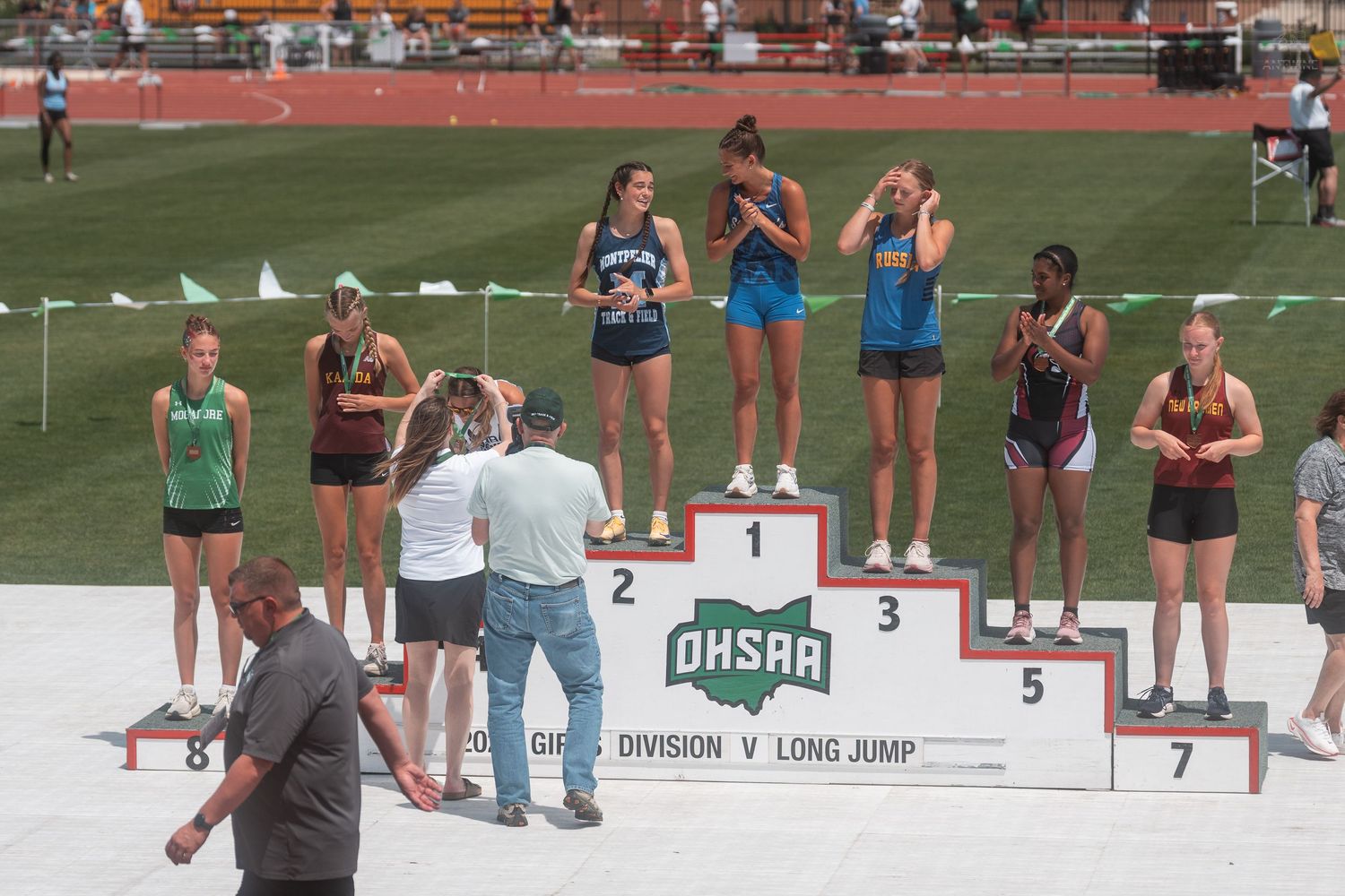 Young female athletes receive medals on the OHSAA Division V Long Jump podium at a state championship.
