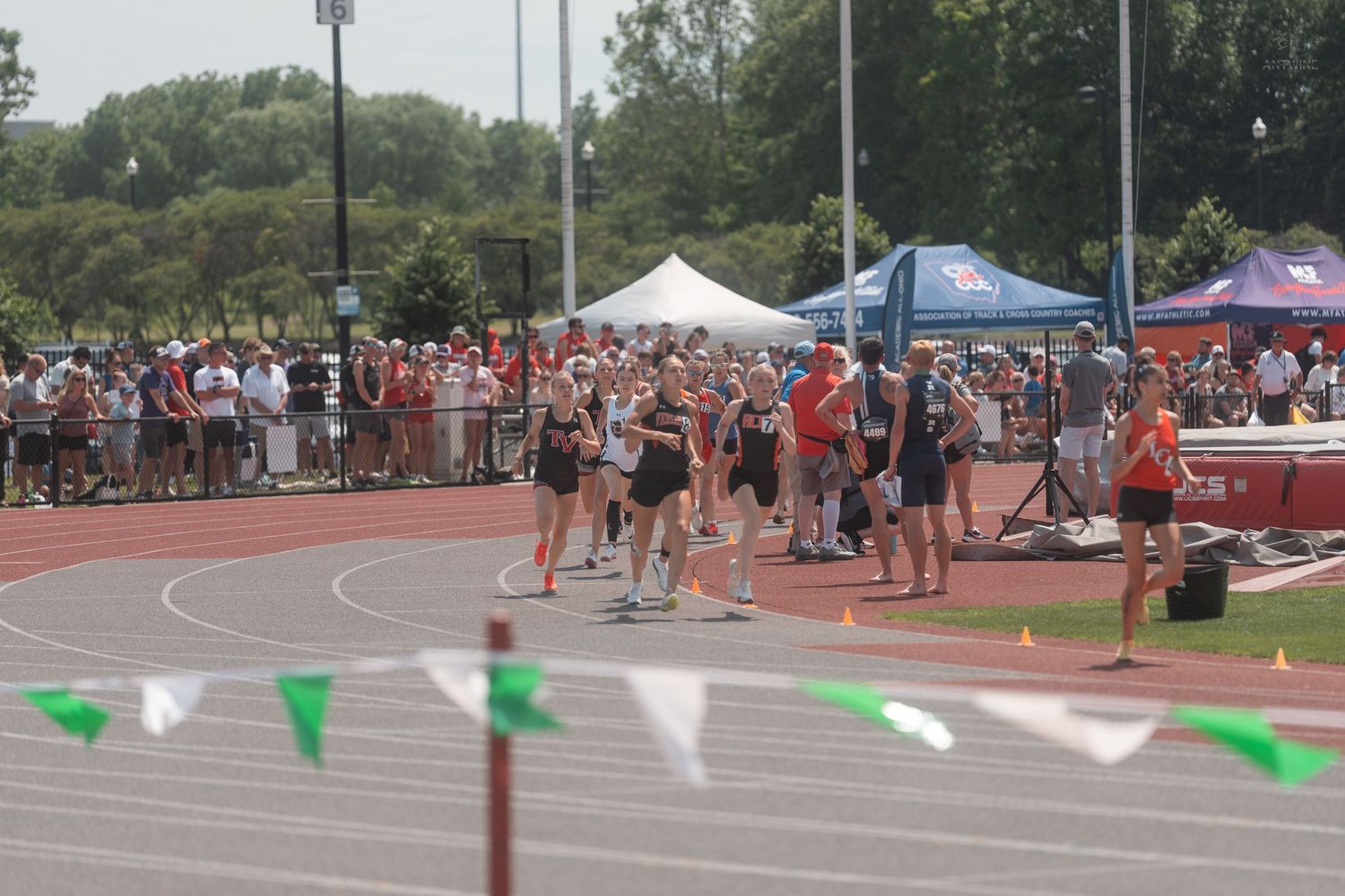 Runners gathering on track at outdoor collegiate track and field meet with spectators.