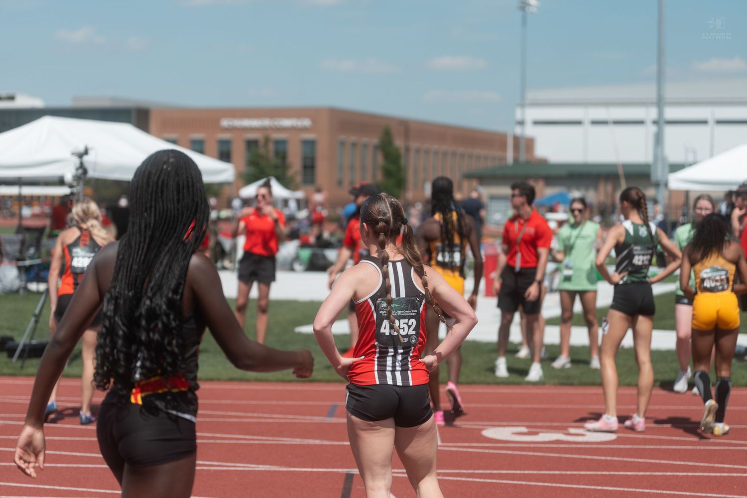 Female track athletes walk on a red track after completing a relay race at a high school meet.
