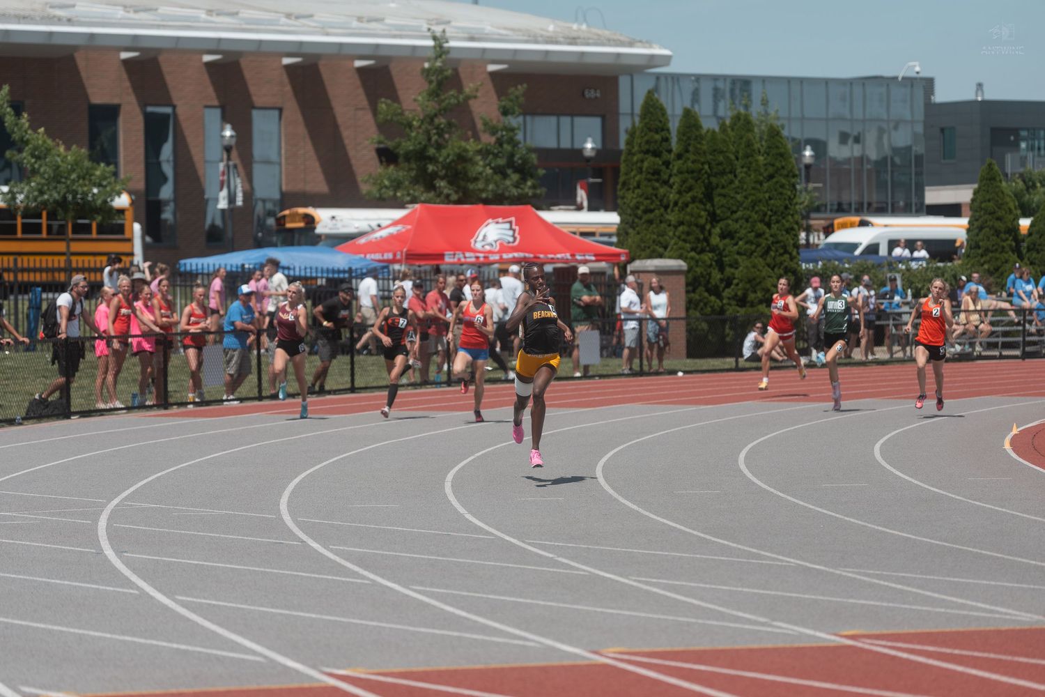 Runners competing on red track during outdoor track and field relay race event.
