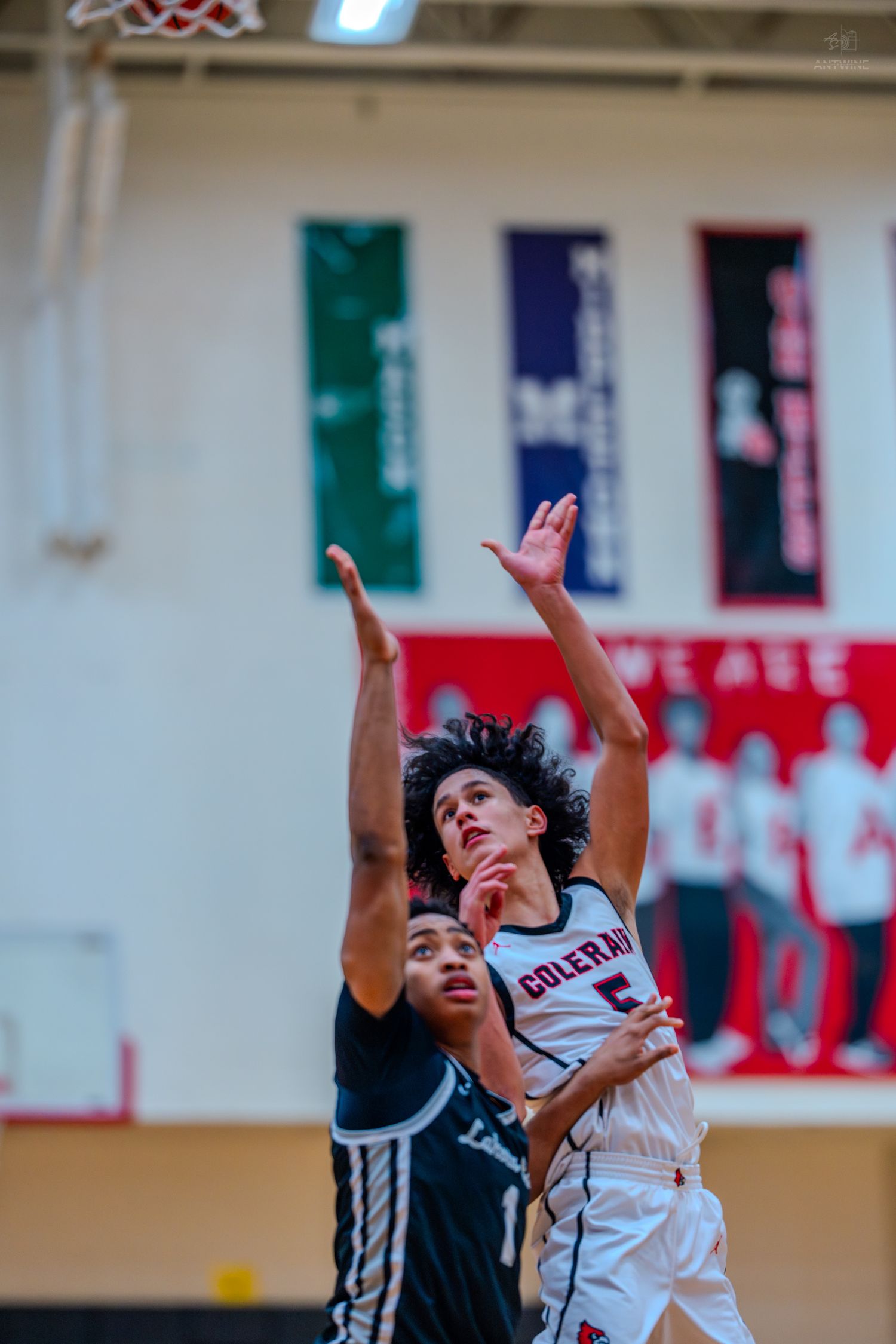 Colerain #5 shoots over a defender during a high school basketball game inside a red gymnasium.