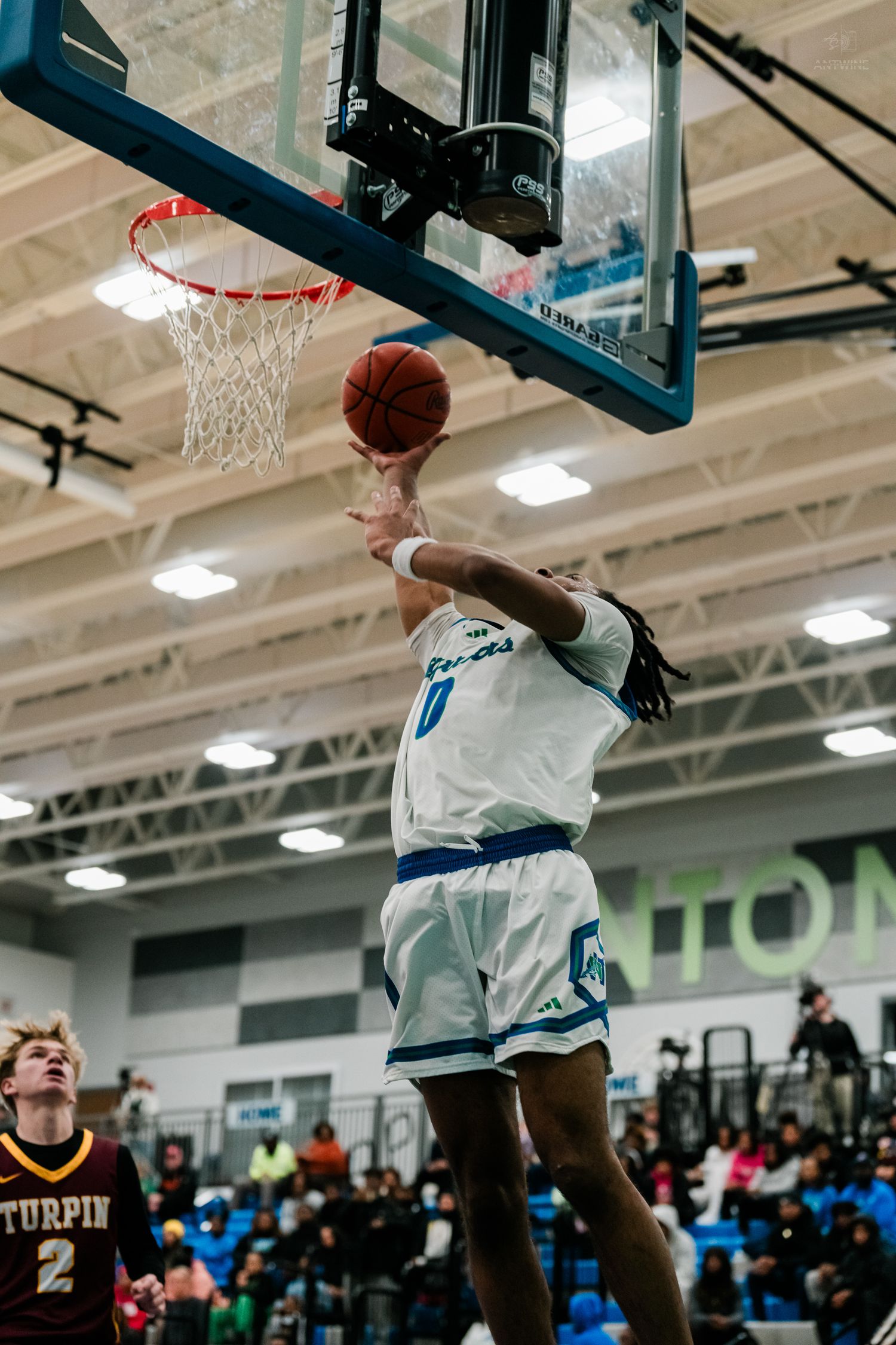 Player #0 in white uniform attempts a layup at the basketball hoop during a high school game against Turpin.