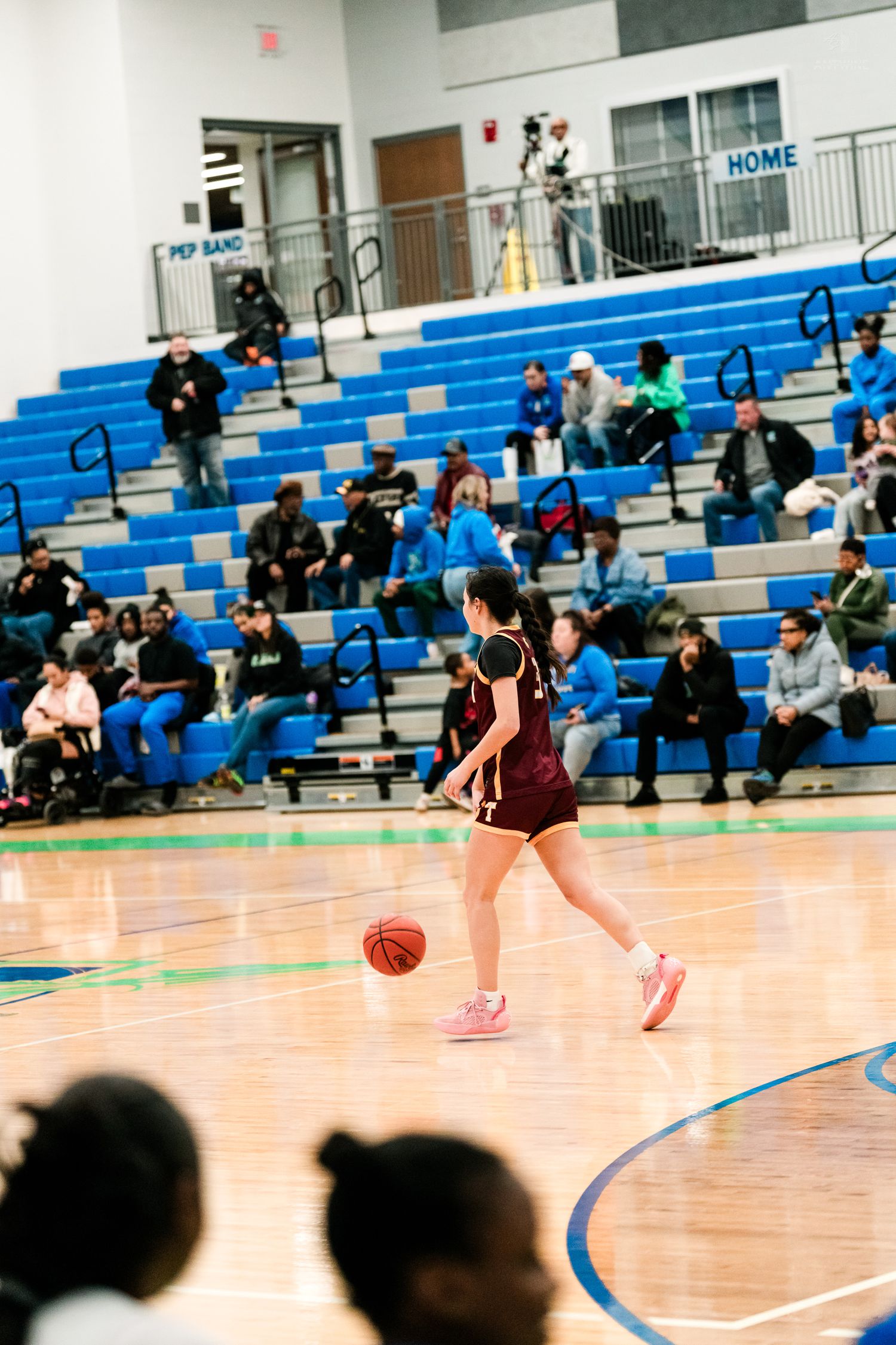 Female high school basketball player in maroon uniform dribbles the ball upcourt in a blue and white gymnasium.