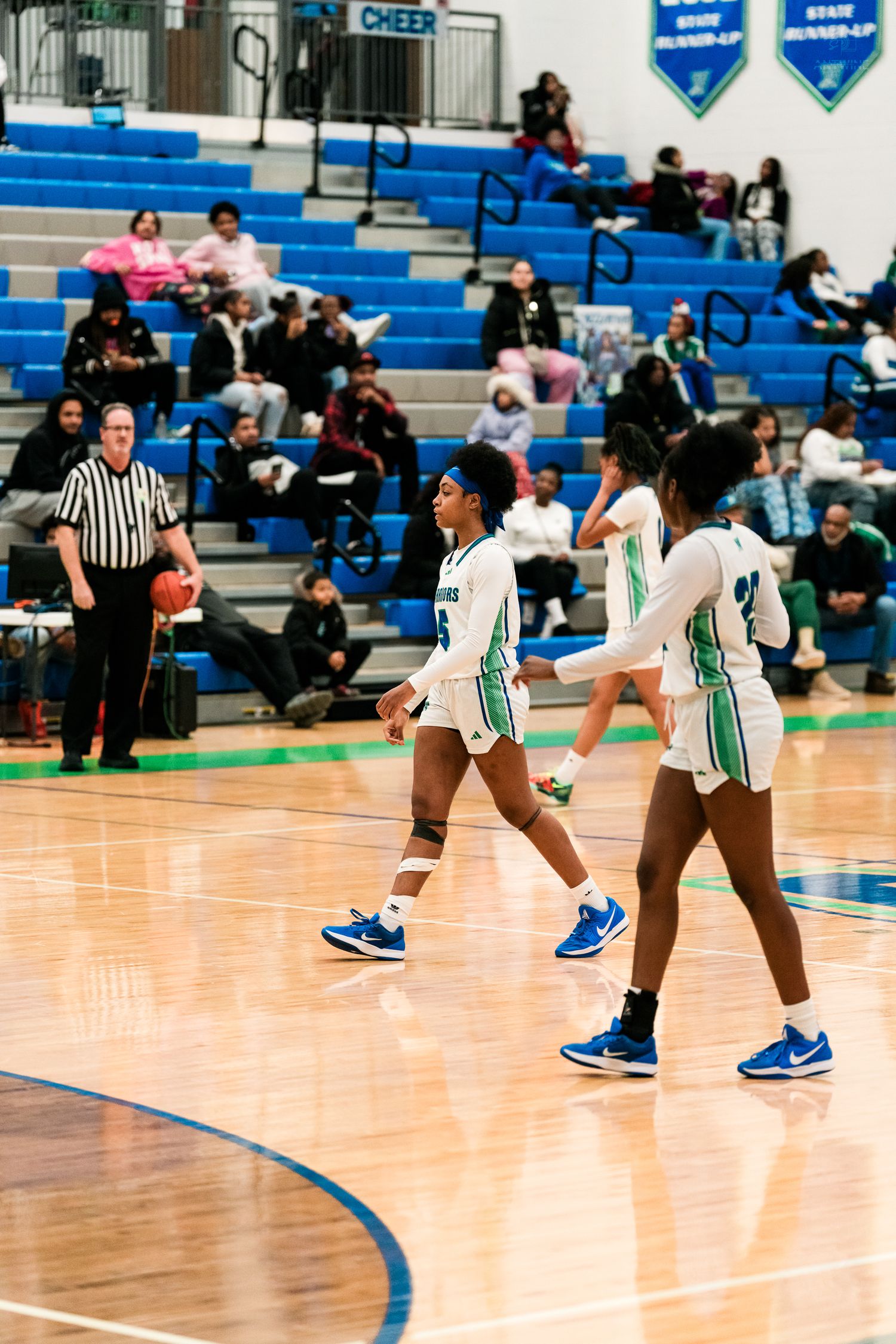 Warriors girls basketball players in white and teal uniforms move on court during high school game.