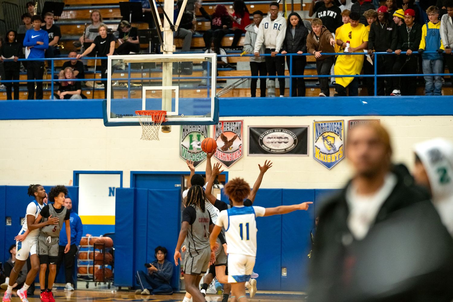 Players compete for a rebound near the basket during an intense high school basketball game in a packed gym.