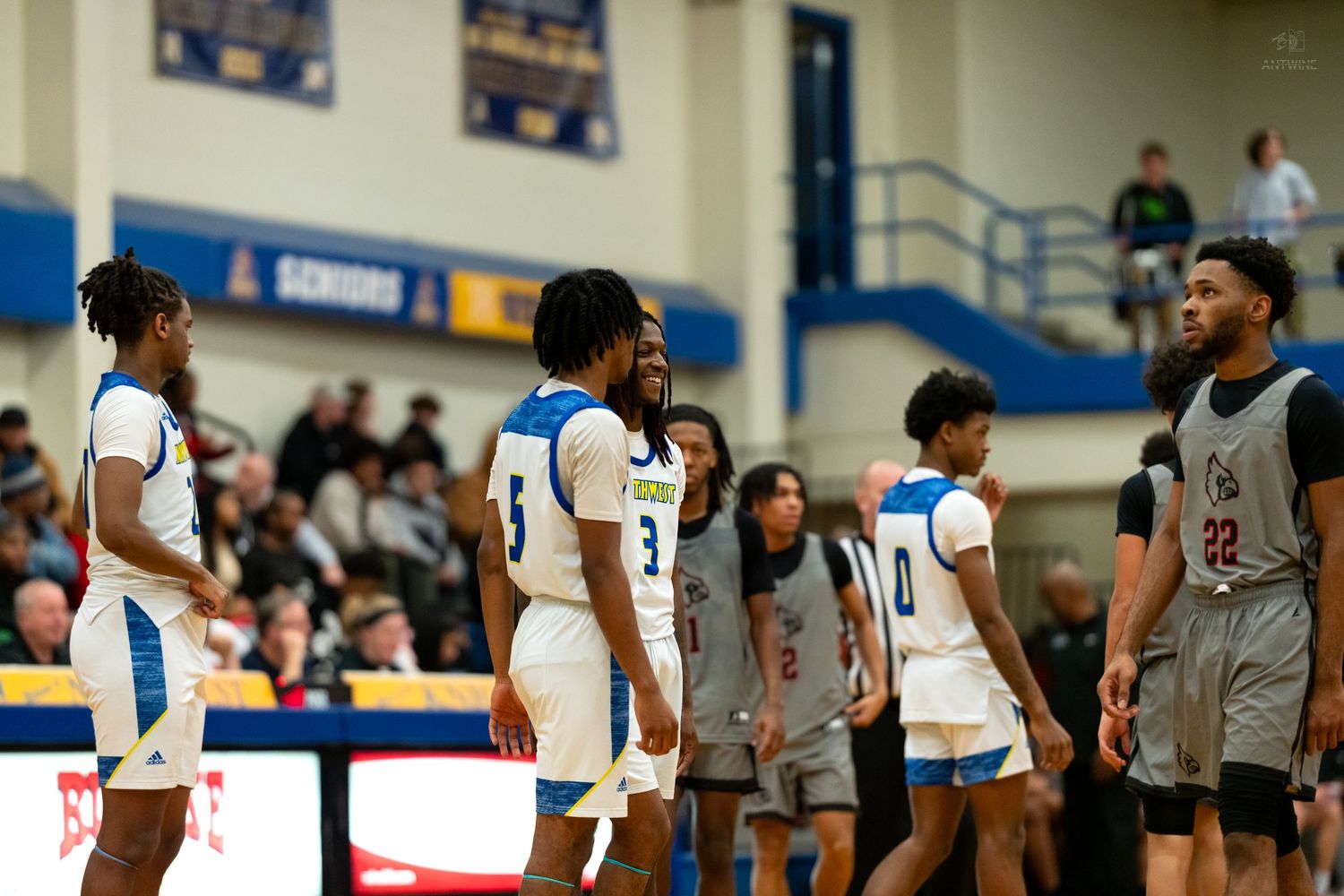 High school basketball players in blue and white uniforms share a laugh during game break.