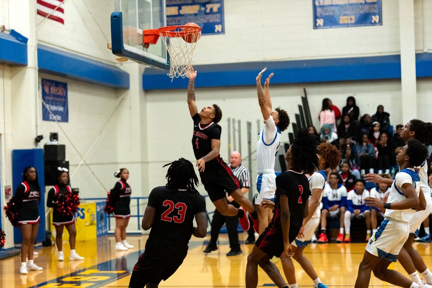 Player #23 in black attempts a dunk over a defender during a high school basketball game.